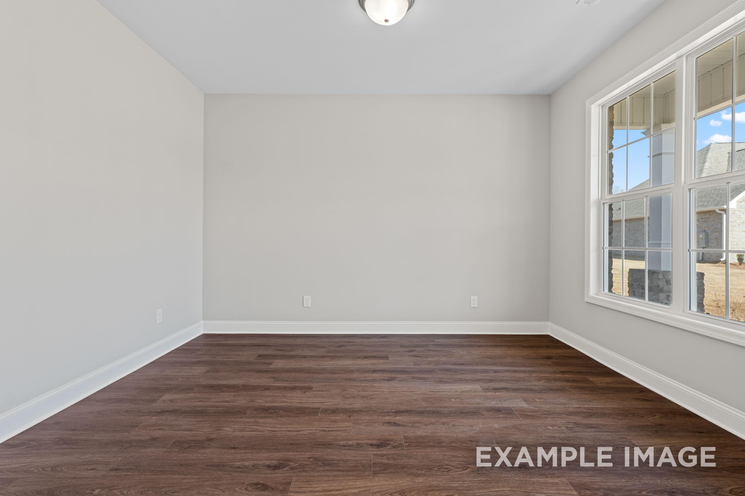 Spacious empty bedroom in The Madison B with light gray walls, dark hardwood floors, and large windows overlooking yard