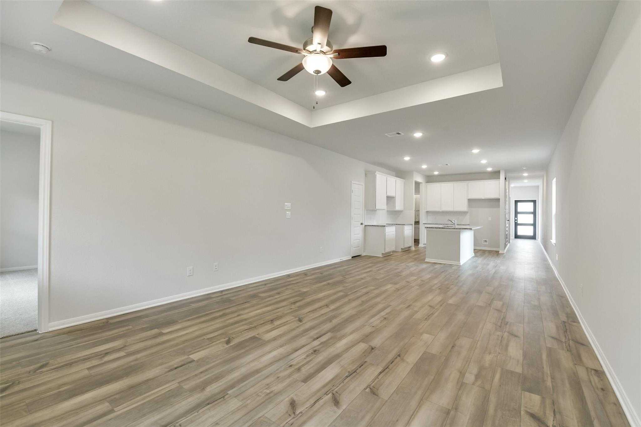Open-concept living and kitchen with white cabinets, hardwood floors, ceiling fan in The Frio G home, Conroe, Texas