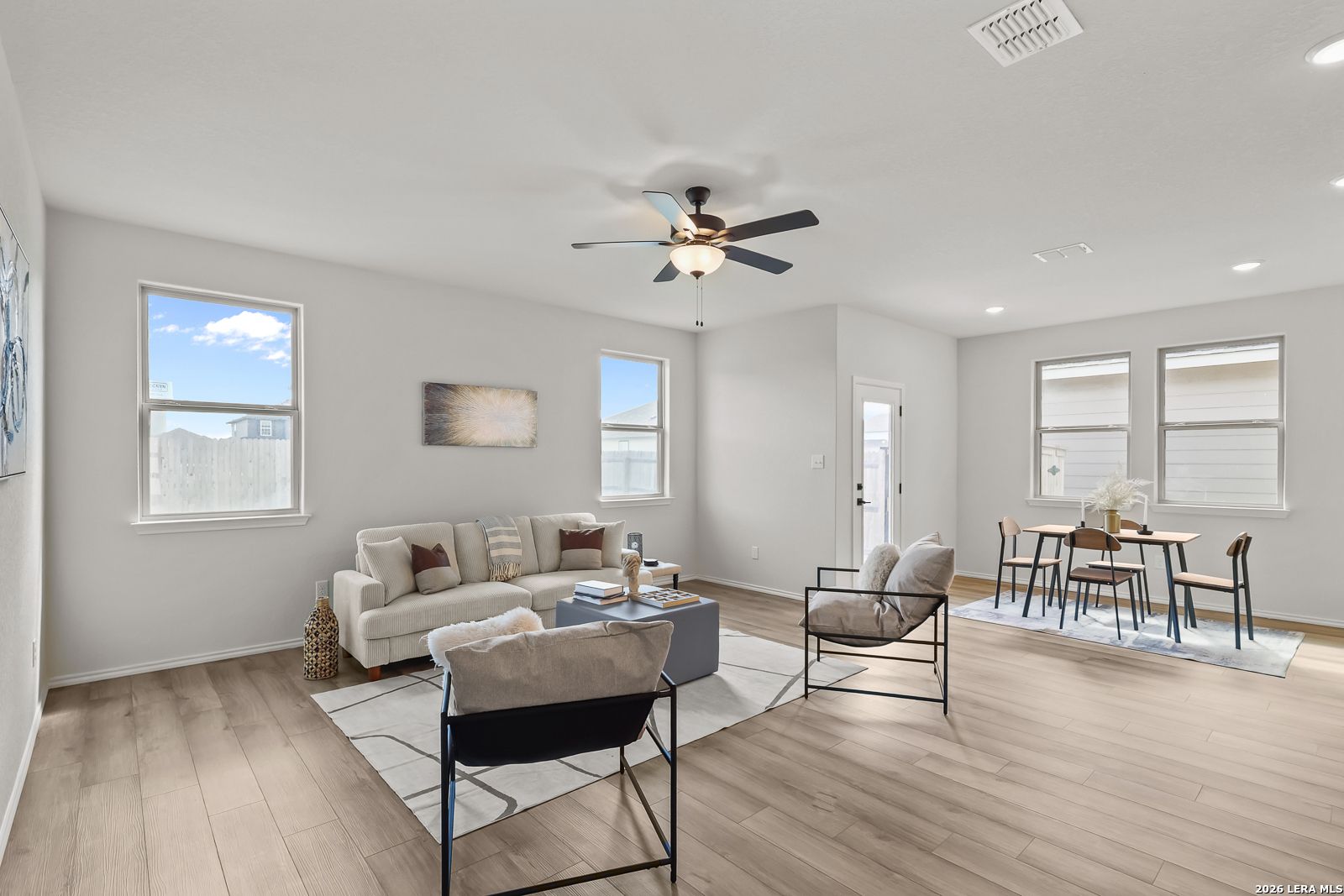 Bright living room with beige sofa, ceiling fan, dining table, and large windows in Davidson Homes The Daphne H, Seguin, Texas