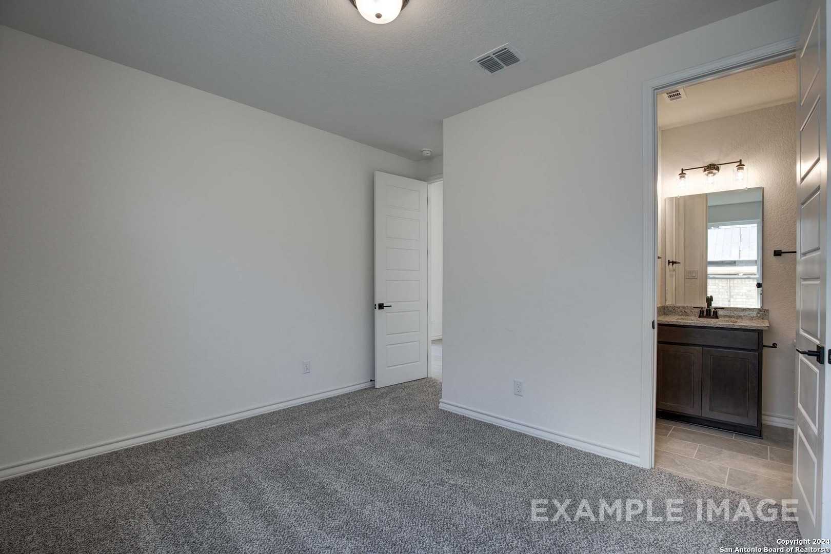 Bright secondary bedroom with adjacent en-suite bath, vanity sink, mirror, and gray carpet in Davidson Homes The Garner C, Castroville, Texas