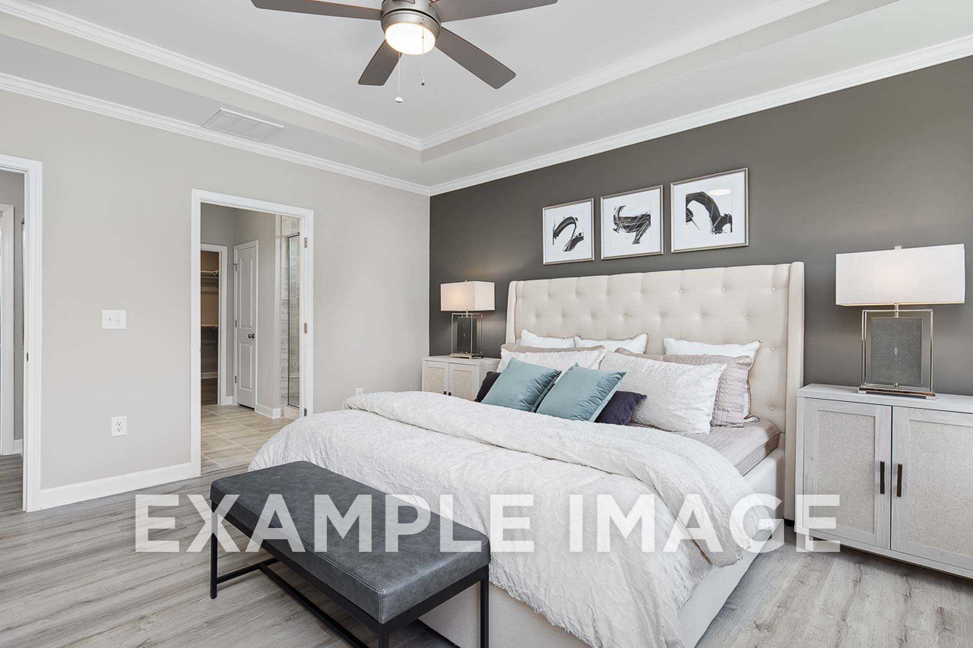 Spacious master bedroom in The Ash E with king bed, beige headboard, ceiling fan, and gray accent wall