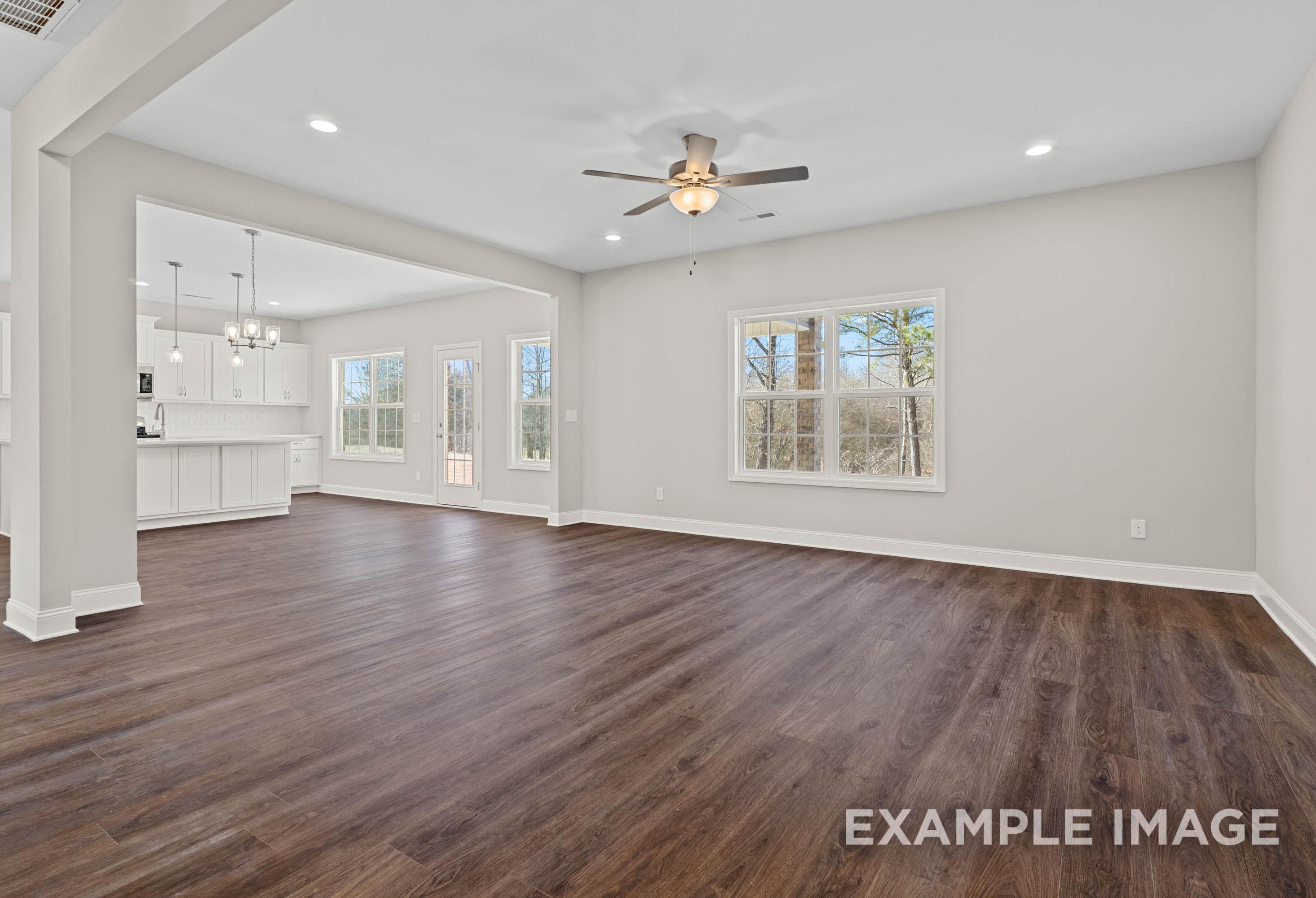 Spacious open-concept living and kitchen in The Madison A home with hardwood floors, large windows, white cabinets, and ceiling fan