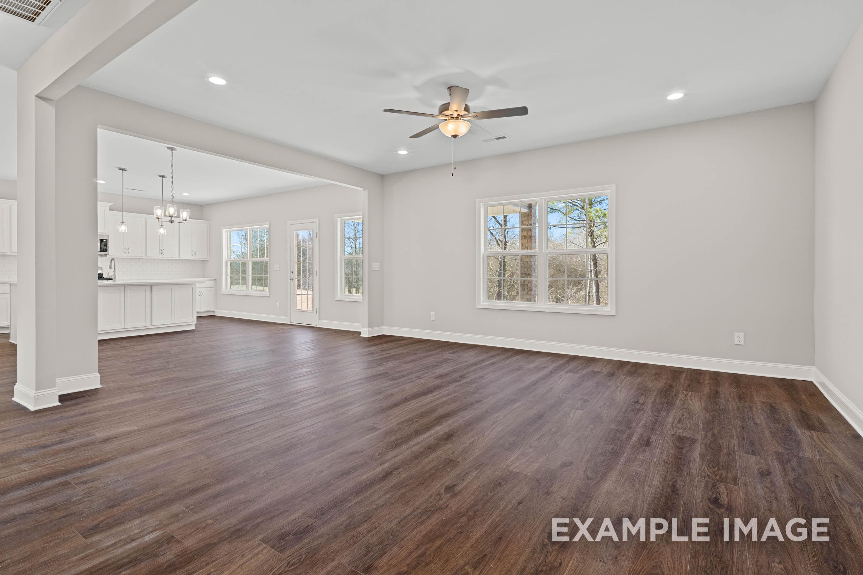 Spacious open-concept living and kitchen in The Madison B with hardwood floors, white cabinets, ceiling fan, and tree-view windows