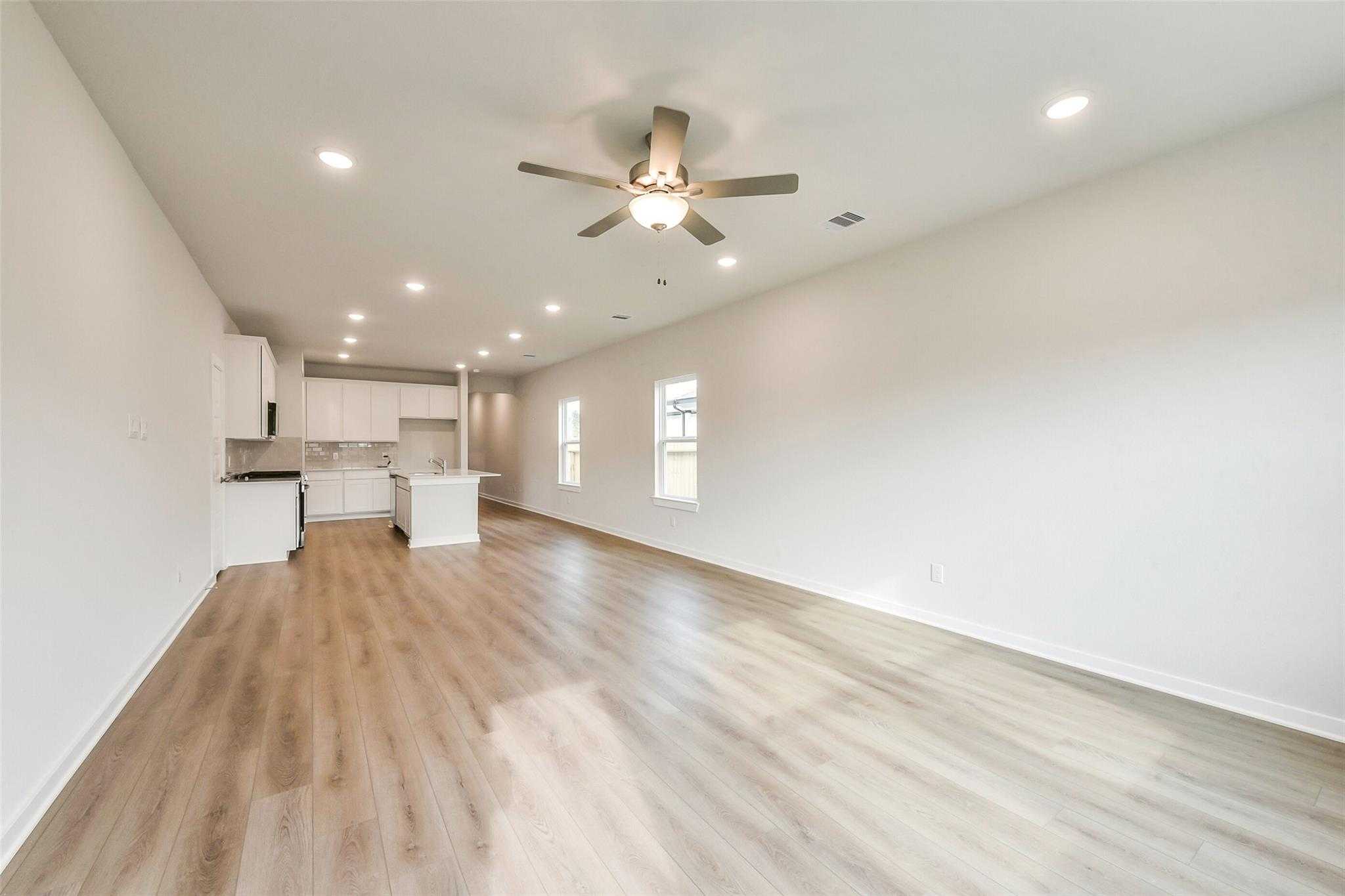 Bright open-concept living room with ceiling fan, recessed lights, and white kitchen island in Davidson Homes The Frio G, Dayton, Texas