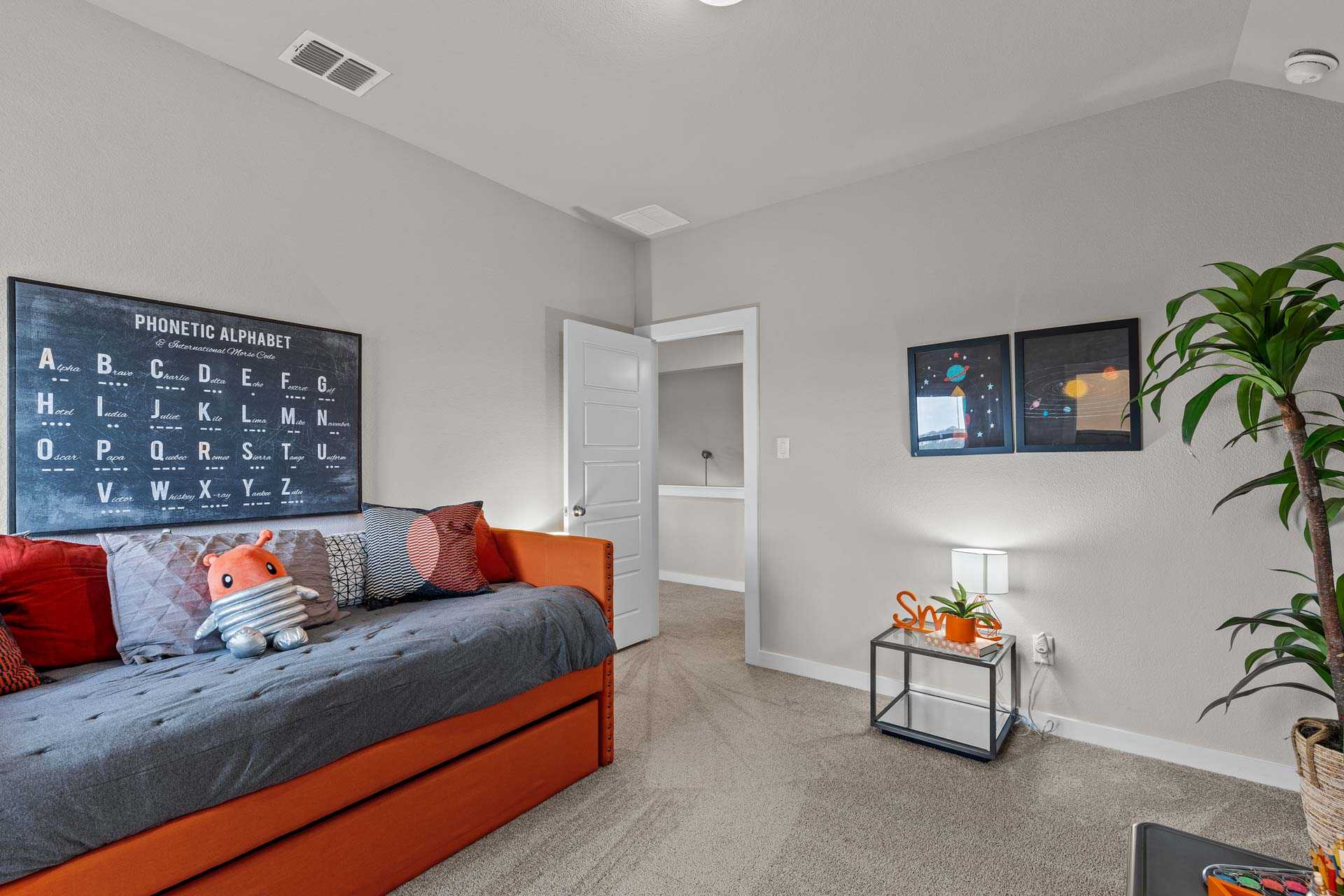 Cozy kids' bedroom in The Collin B home with phonetic alphabet poster, gray daybed, orange pillows, and potted plant