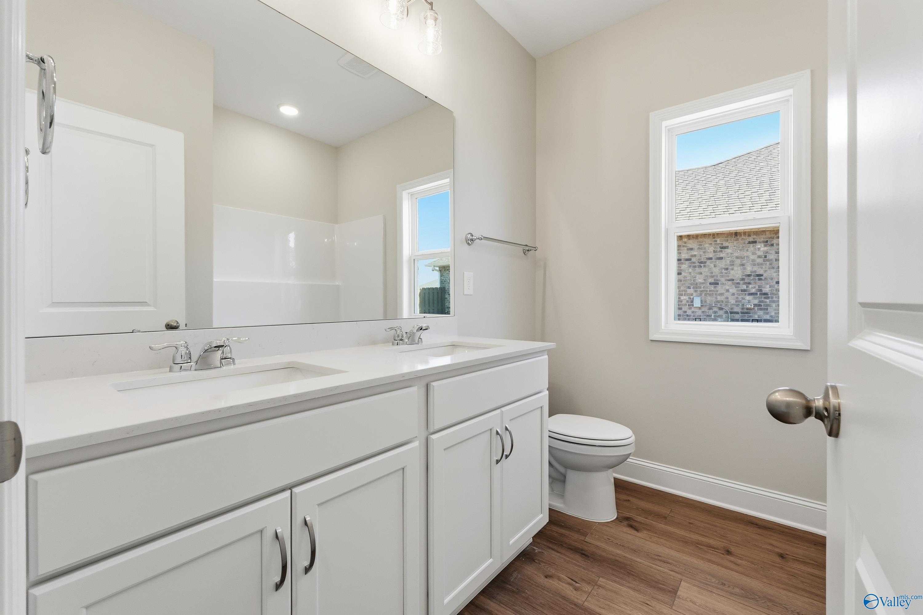 Modern double-sink bathroom with white quartz vanity, large mirror, and window in Davidson Homes The Everett, Harvest, Alabama