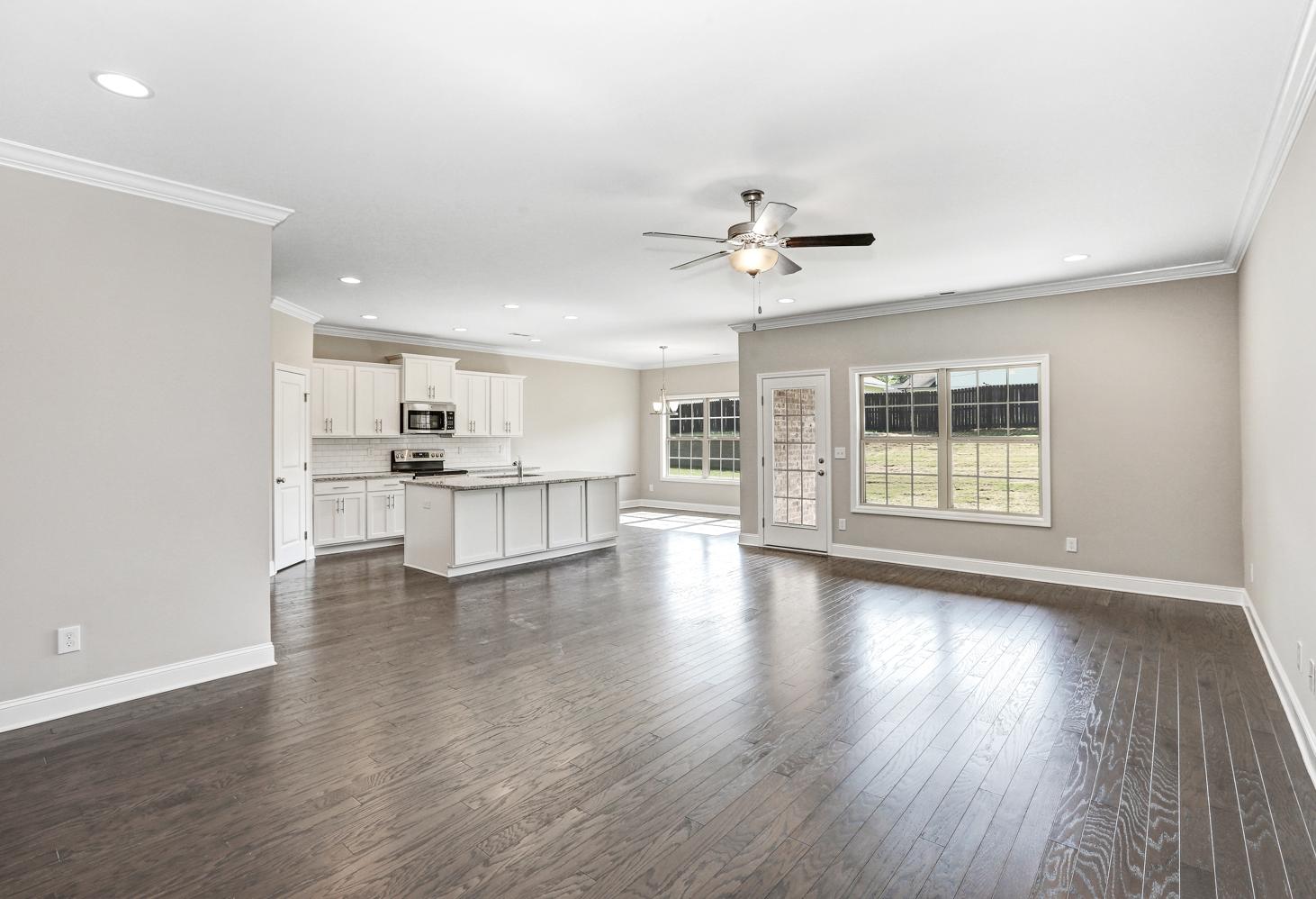 Spacious open-concept kitchen in The Montgomery home with white cabinets, large island, ceiling fan, and hardwood floors