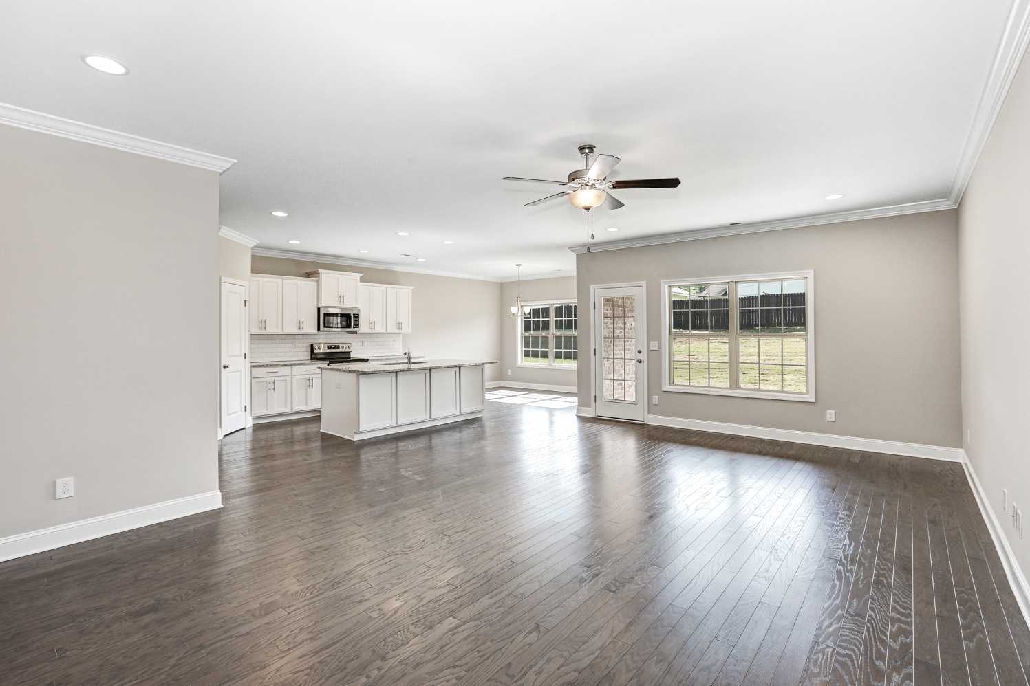 Spacious open-concept kitchen in The Montgomery home with white cabinets, large island, ceiling fan, and hardwood floors