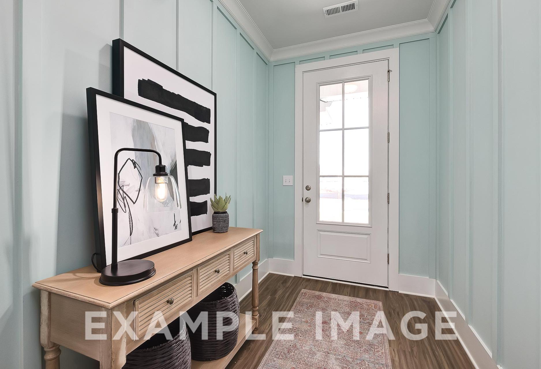Spacious entryway in The Everett B with light blue paneled walls, white French door, wooden console table, abstract art, and potted plant