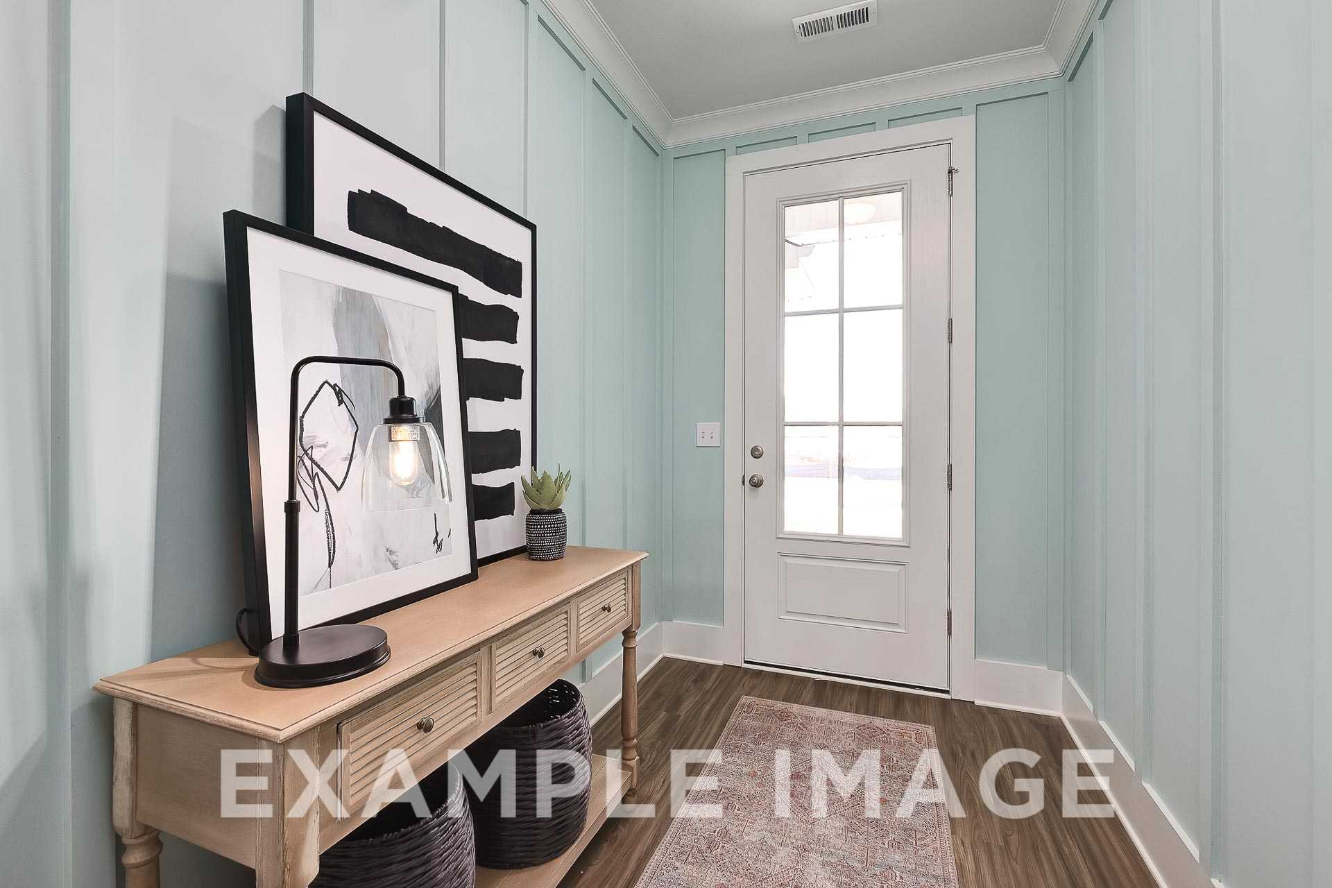 Spacious entryway in The Everett B with light blue paneled walls, white French door, wooden console table, abstract art, and potted plant