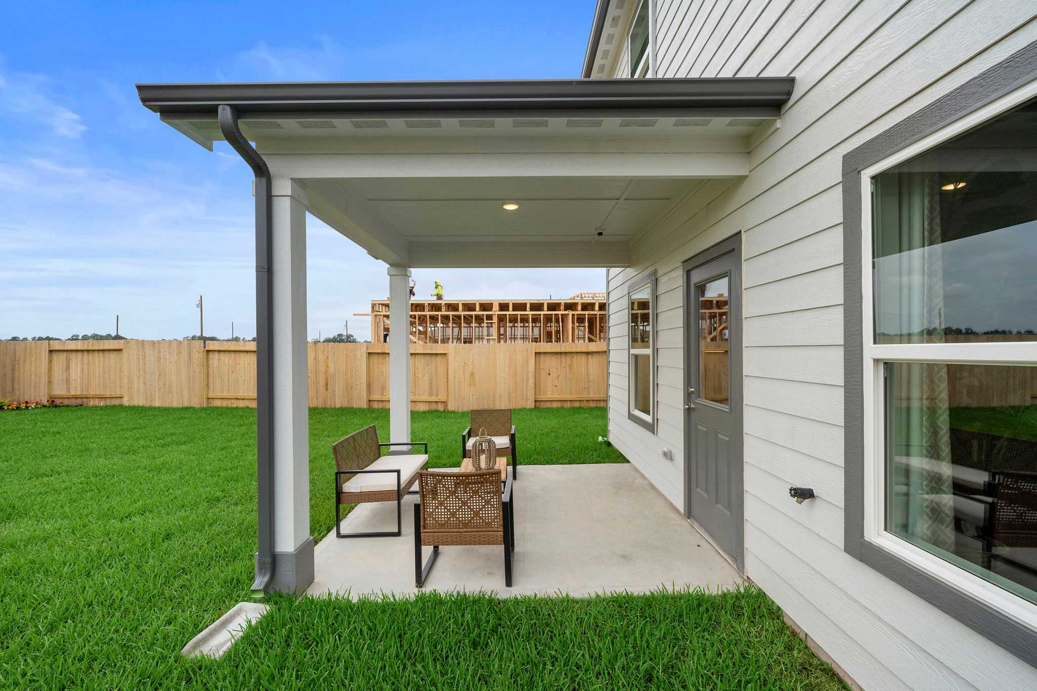 Covered patio with wicker seating at Spring Branch Crossing home in Conroe Texas, white siding, green lawn, wooden fence
