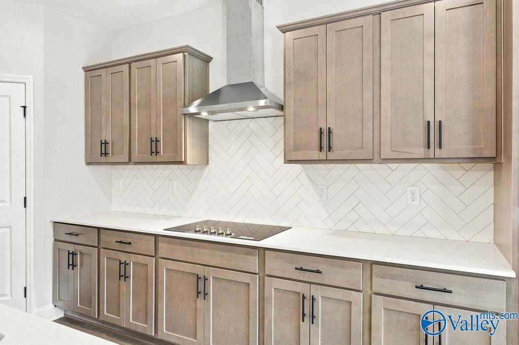 Modern kitchen with weathered wood cabinets, herringbone tile backsplash, and stainless range hood in The Rockford by Davidson Homes, Hartselle
