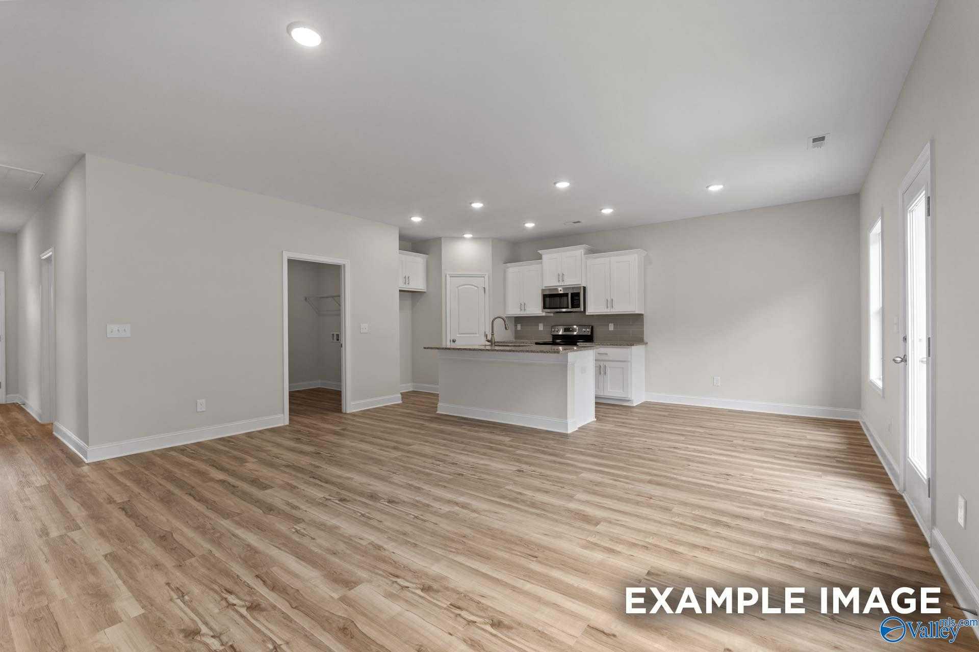Open-concept kitchen with white cabinets, island sink, hardwood floors, and large windows in Davidson Homes The Butler, Toney, Alabama
