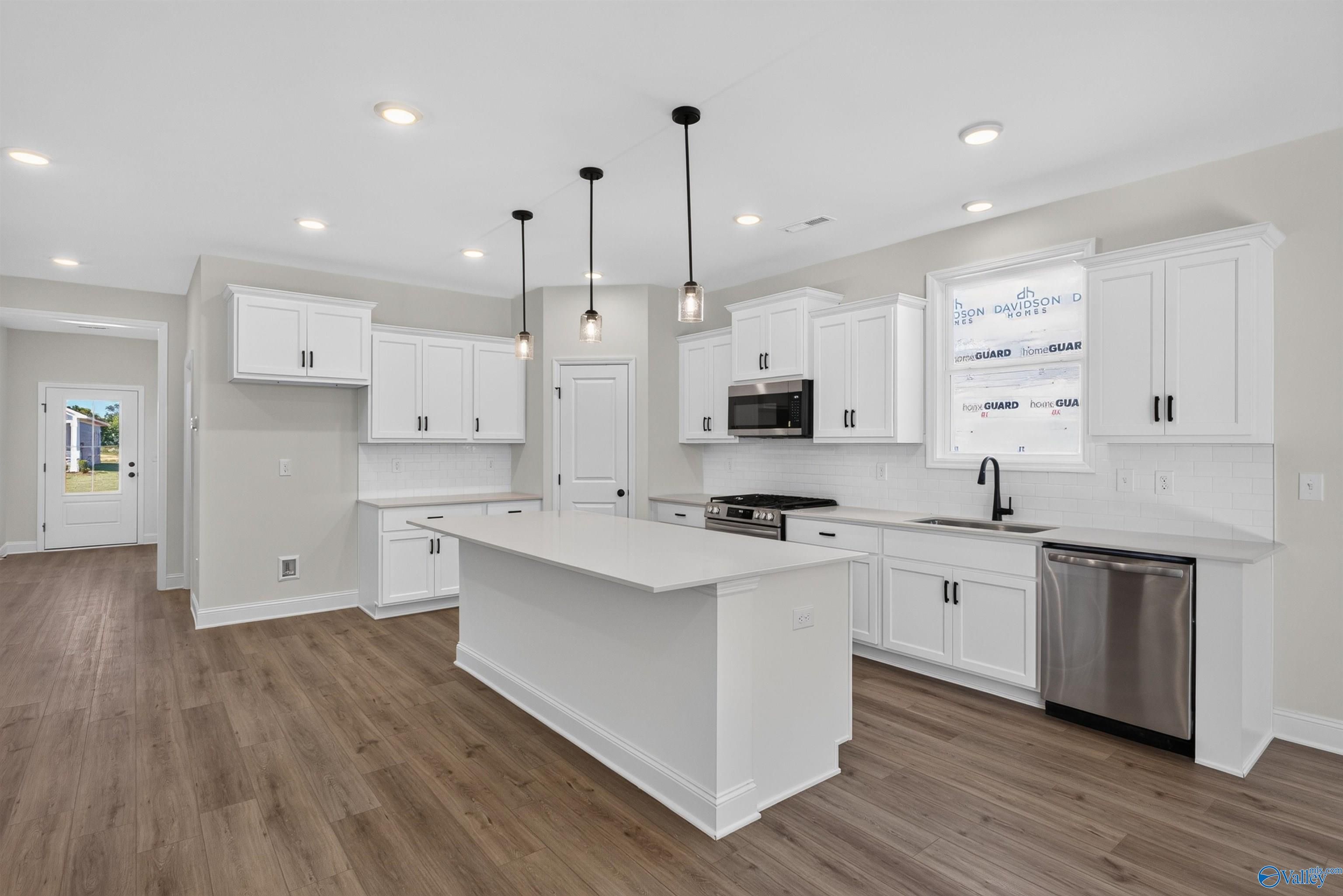 White kitchen with large island, pendant lights, and stainless appliances in Davidson Homes Ashport L, Berry Cove, New Market, AL