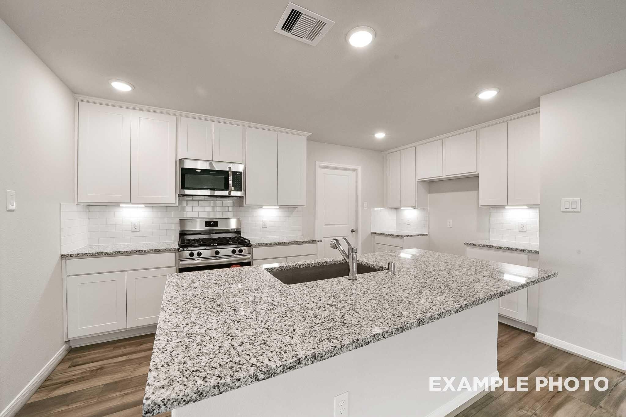 Modern white kitchen with granite island, stainless appliances, recessed lighting in Davidson Homes Tierra B, Beasley, Texas