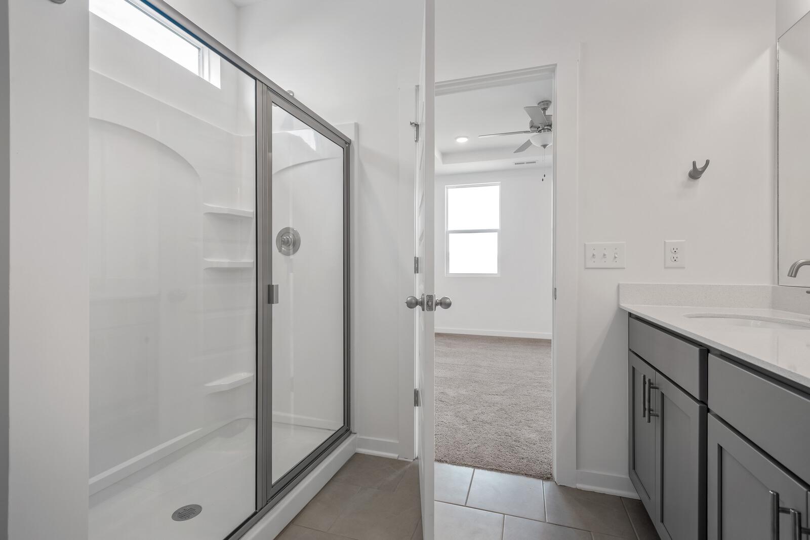 Modern master bathroom in The Asheville with frameless glass shower, arched tile enclosure, and sleek dark vanity