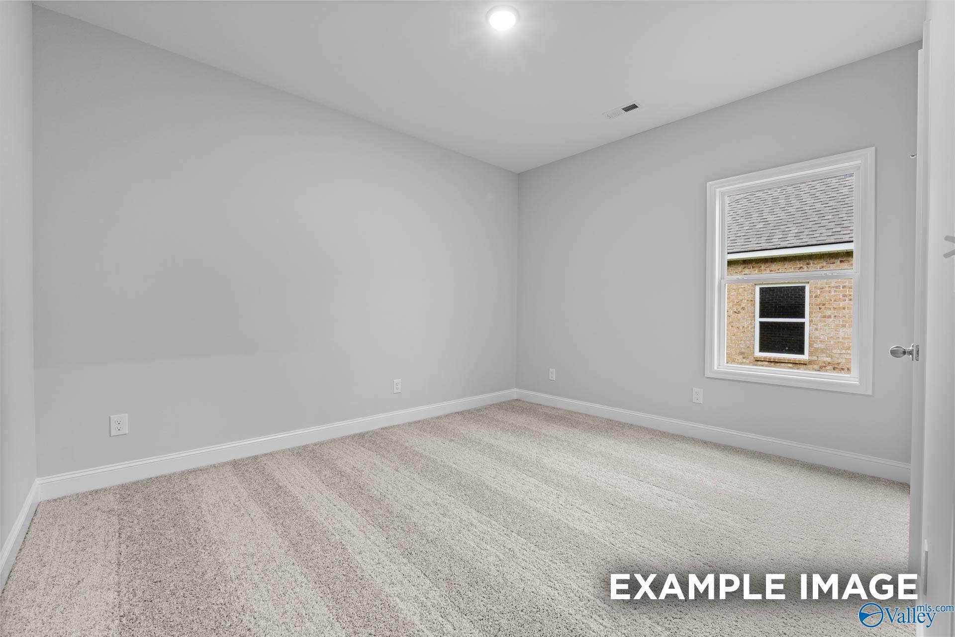 Empty bedroom with light gray walls, beige carpet, and window overlooking exterior in The Daphne 4-bedroom home, Meridianville, Alabama