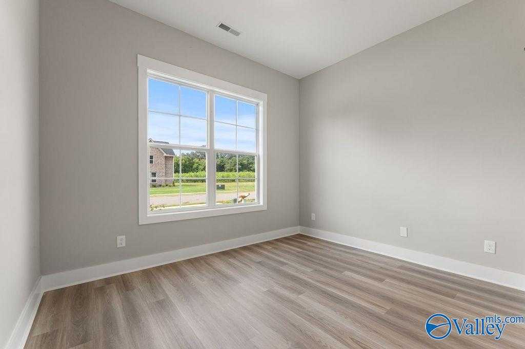 Bright empty bedroom with gray walls, large window overlooking suburban view, and laminate wood floors in Evermore Homes The Oxford, Owens Cross Roads, AL
