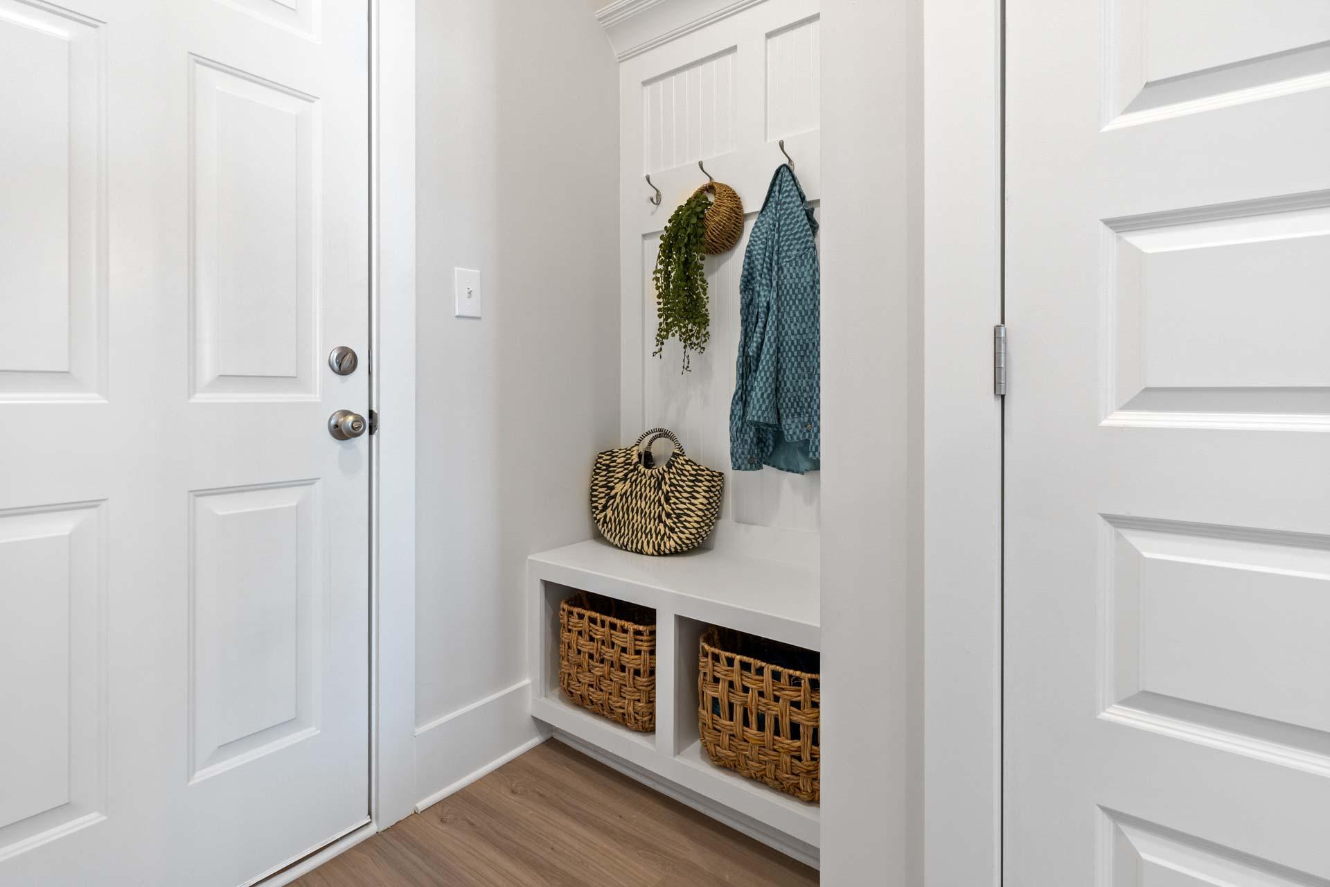 White mudroom with built-in bench, coat hooks, hanging plants, turquoise jacket, and wicker baskets at Walker's Hill in Meridianville, Alabama
