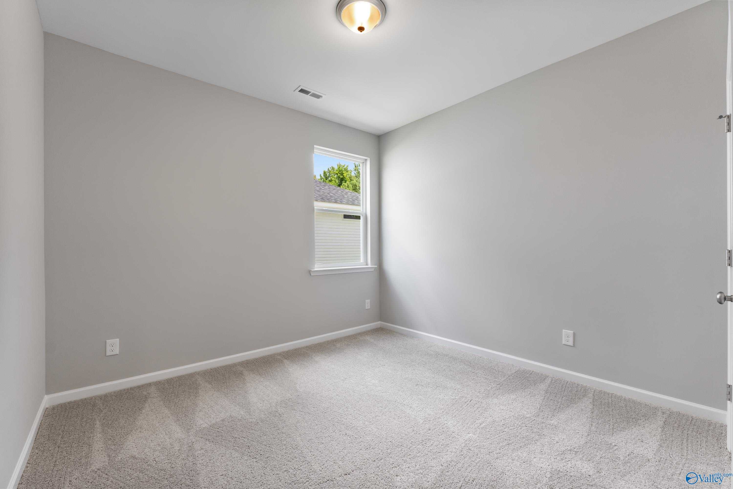 Empty bedroom with gray walls, beige carpet, window overlooking trees in Davidson Homes The Phoenix, Hazel Green, Alabama
