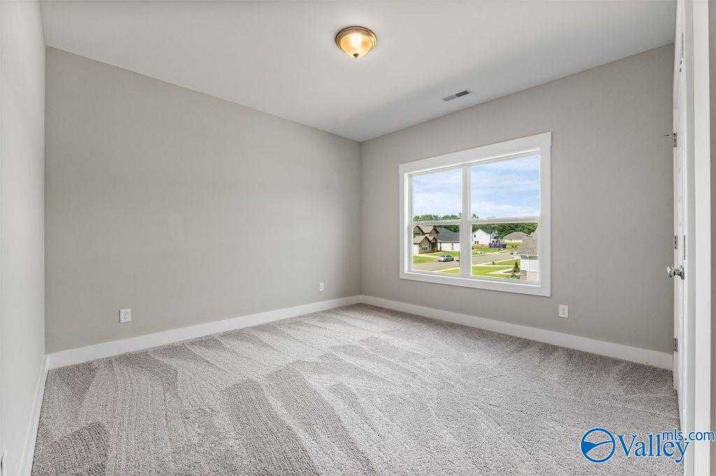 Empty bedroom with gray walls, plush carpet, large window overlooking neighborhood in Evermore Homes The Oxford, Owens Cross Roads, Alabama