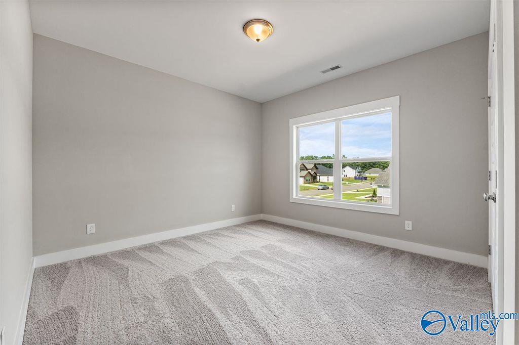 Bright empty bedroom with gray walls, carpet flooring, and large window overlooking neighborhood in The Oxford home, Owens Cross Roads, AL