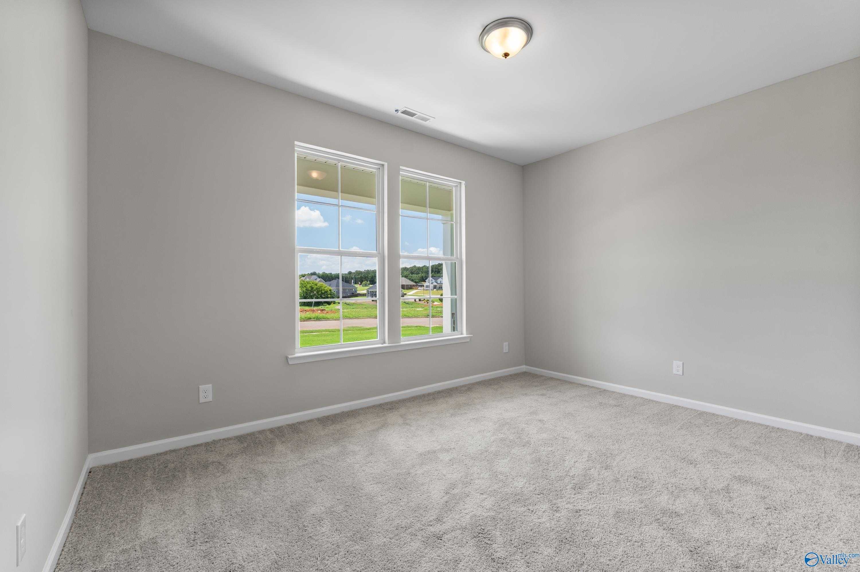 Bright secondary bedroom with light gray walls, carpeted floor, and large windows overlooking green yard in Davidson Homes The Sanctuary, Huntsville