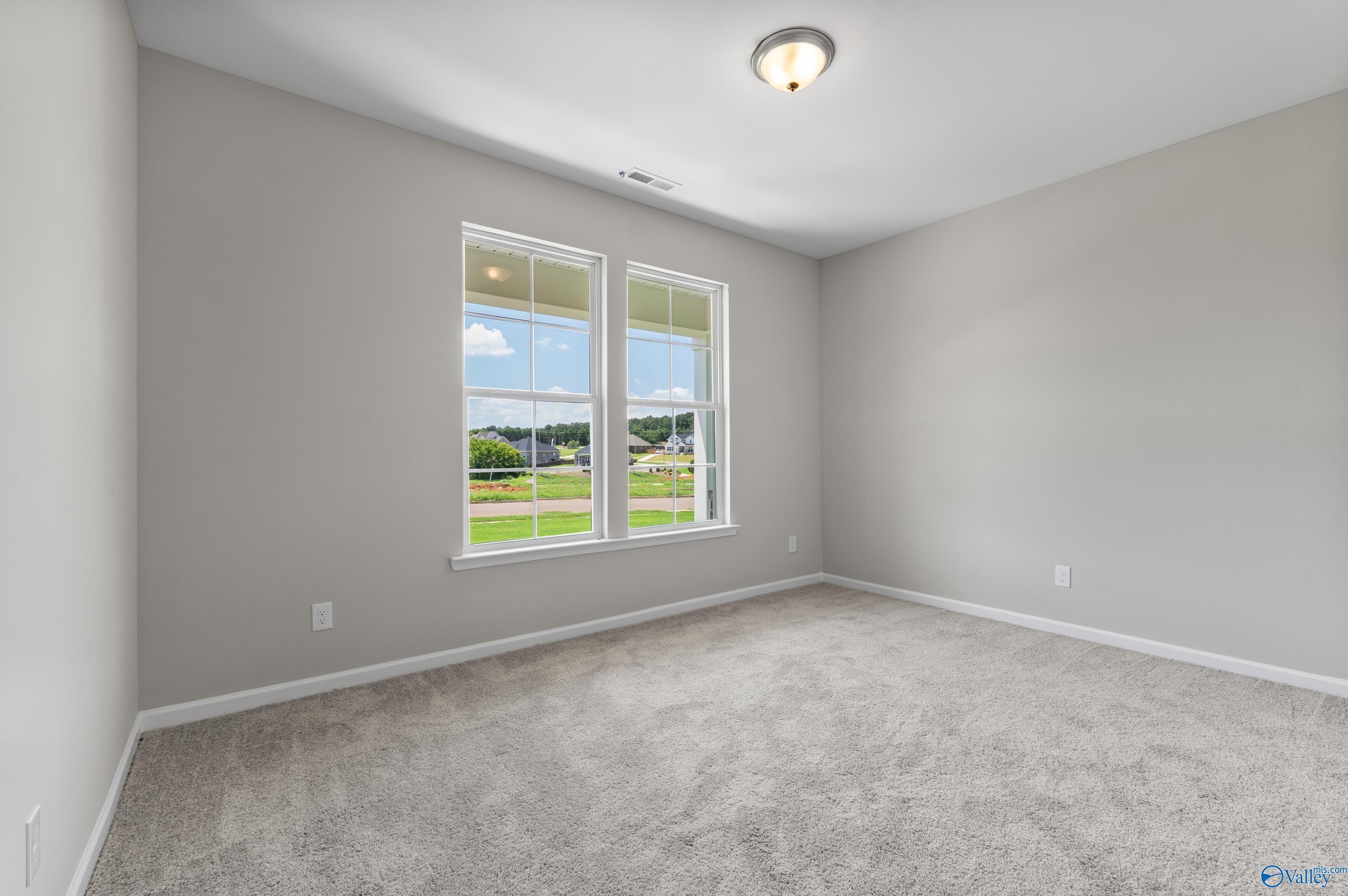 Bright bedroom with gray walls, carpet floor, and large windows overlooking green yard in Davidson Homes The Sanctuary, Huntsville, AL