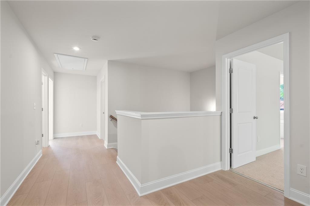 Upstairs hallway with oak hardwood floors, white railing overlook, and bedroom doors in The Hickory E 5-bedroom home, Buford, Georgia