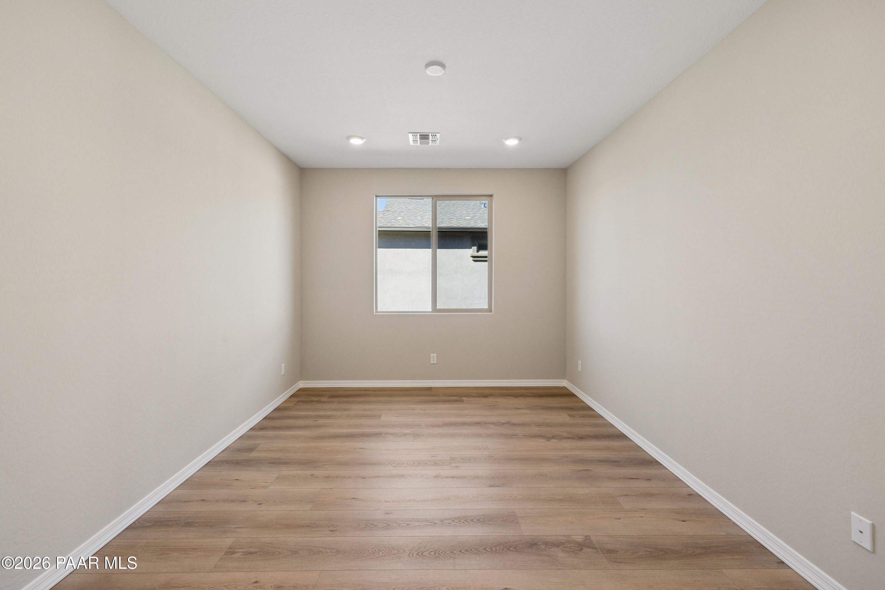 Empty bedroom featuring beige walls, light hardwood floors, and large window in Davidson Homes The Harmony A, Prescott Valley, AZ