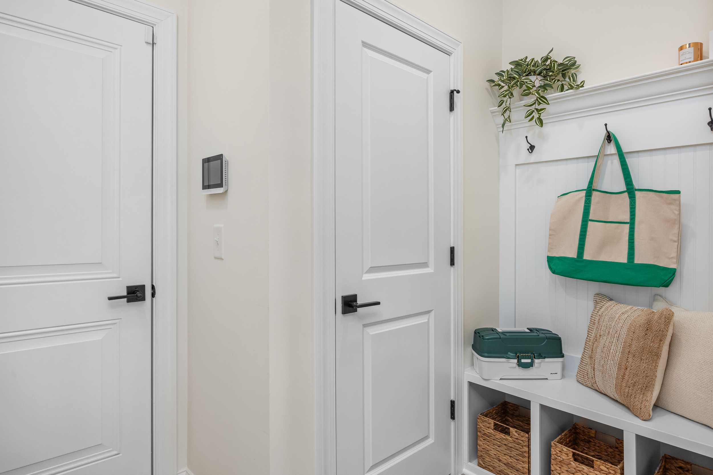 Functional mudroom with white doors, built-in beige bench, wicker baskets, hanging totes and plant at Laneridge Estates Raleigh NC