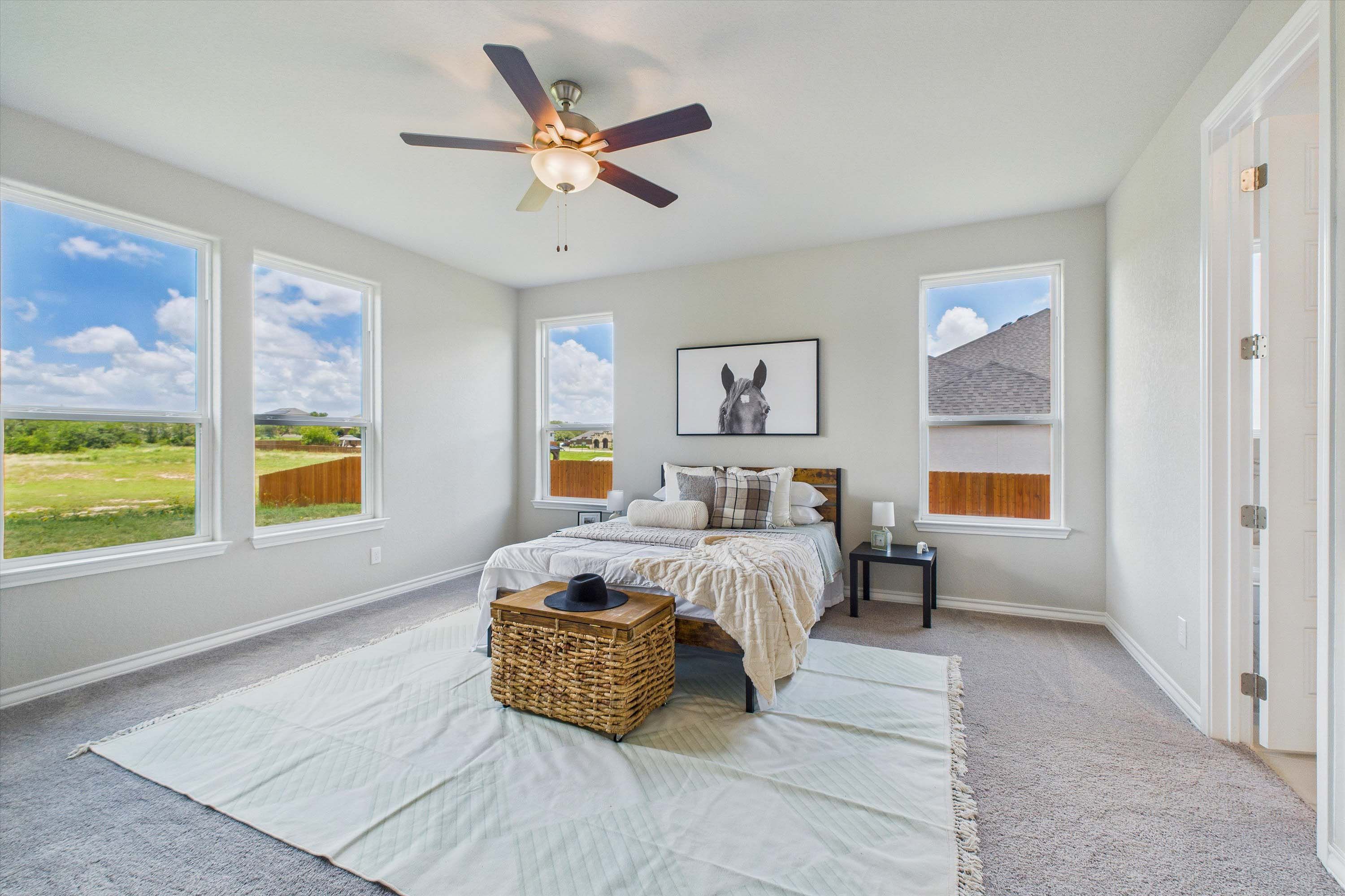 Spacious master suite in The Foster featuring large windows, neutral decor, and modern ceiling fan in Castroville, Texas.
