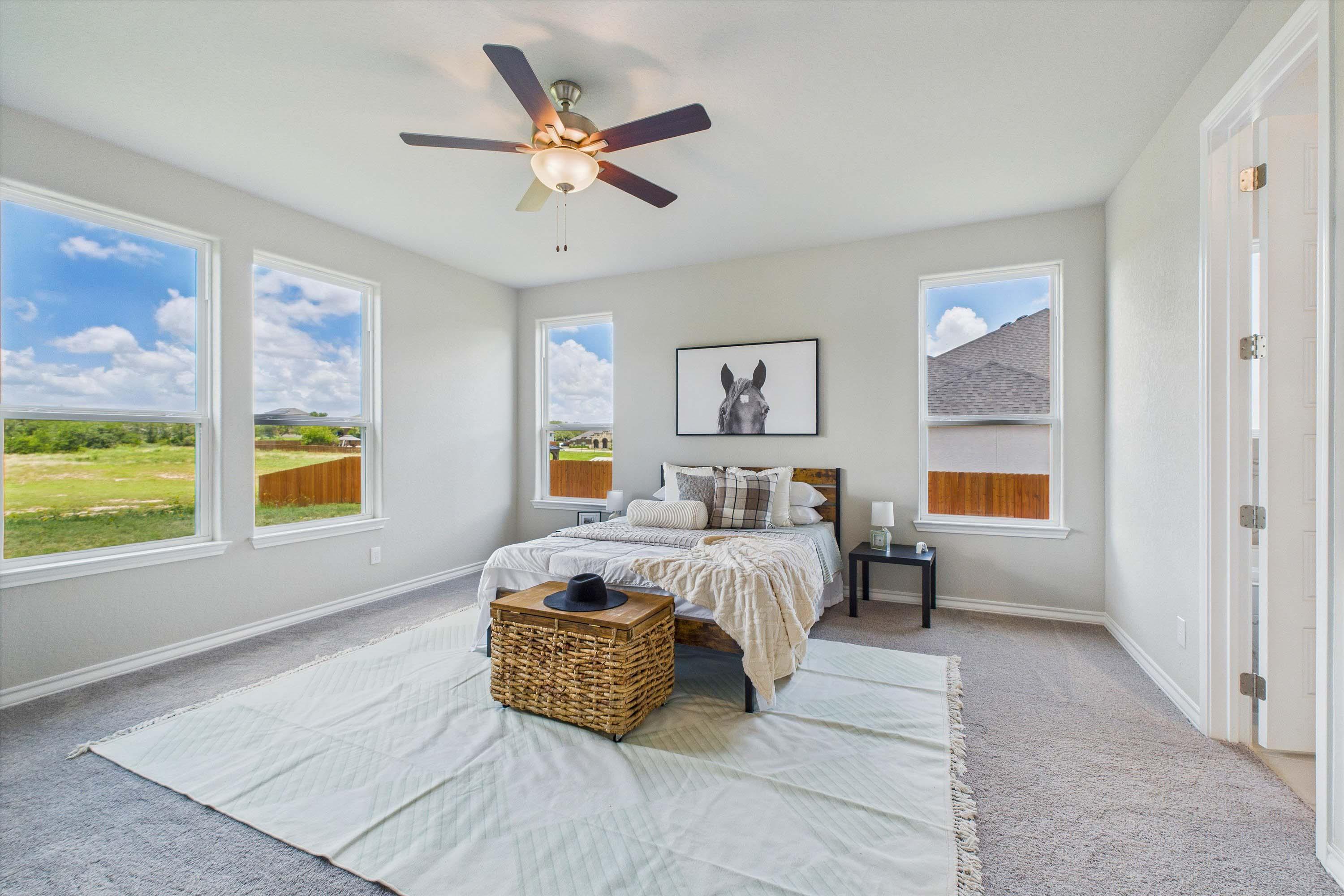 Spacious master suite in The Foster featuring large windows, neutral decor, and modern ceiling fan in Castroville, Texas.