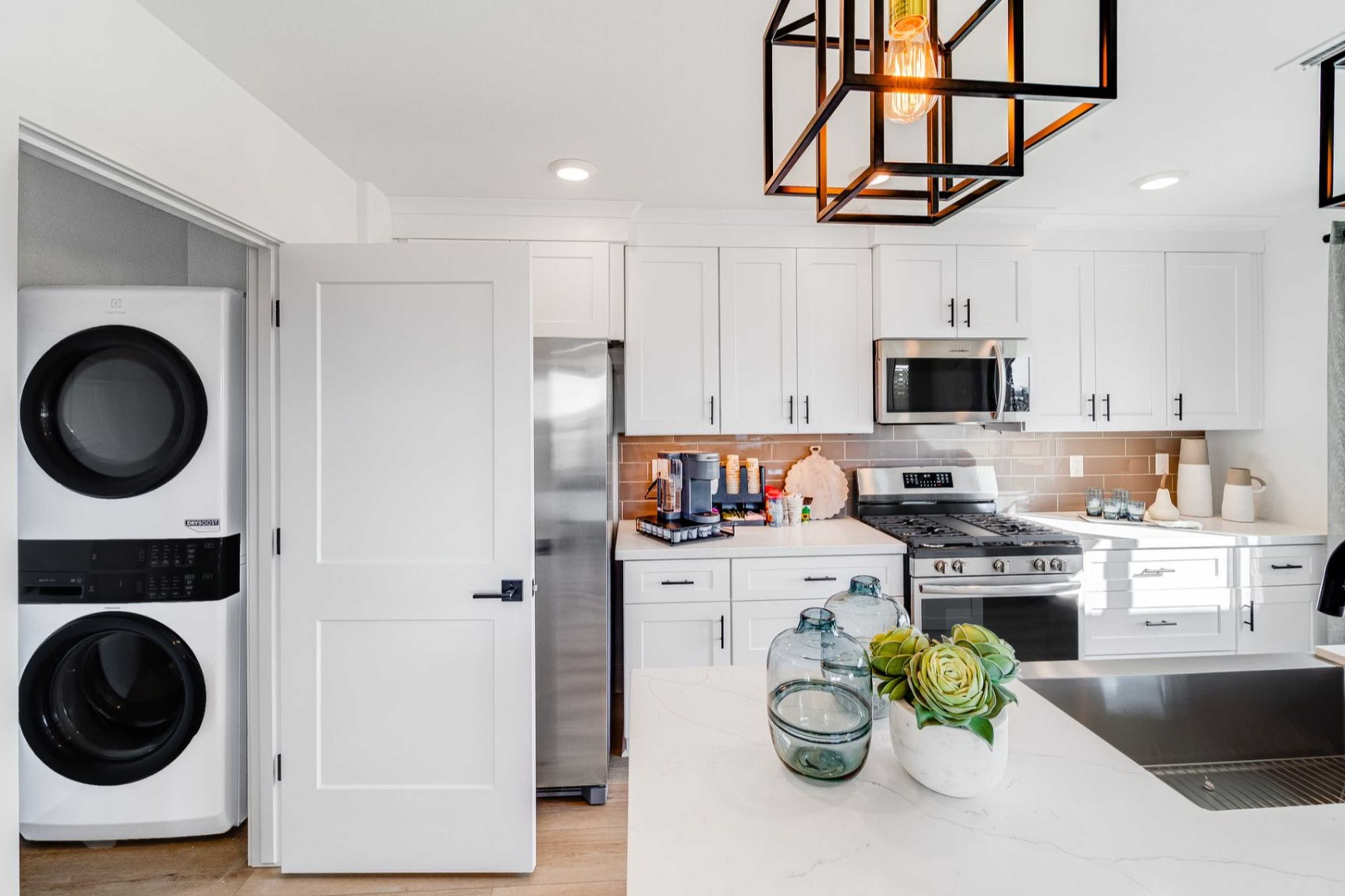 Spacious laundry room with stacked white washer dryer next to modern kitchen in The Wilmington B, featuring quartz counters and stainless appliances