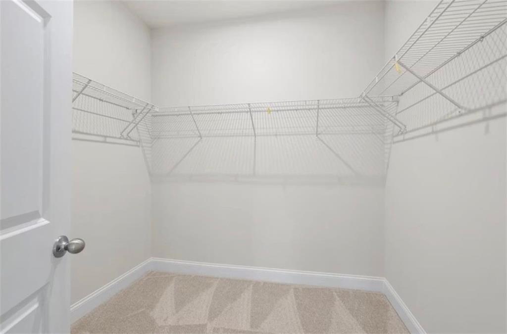 Walk-in closet with white wire shelving and plush carpet in The Ash C floor plan at Wehunt Meadows, Hoschton, Georgia.