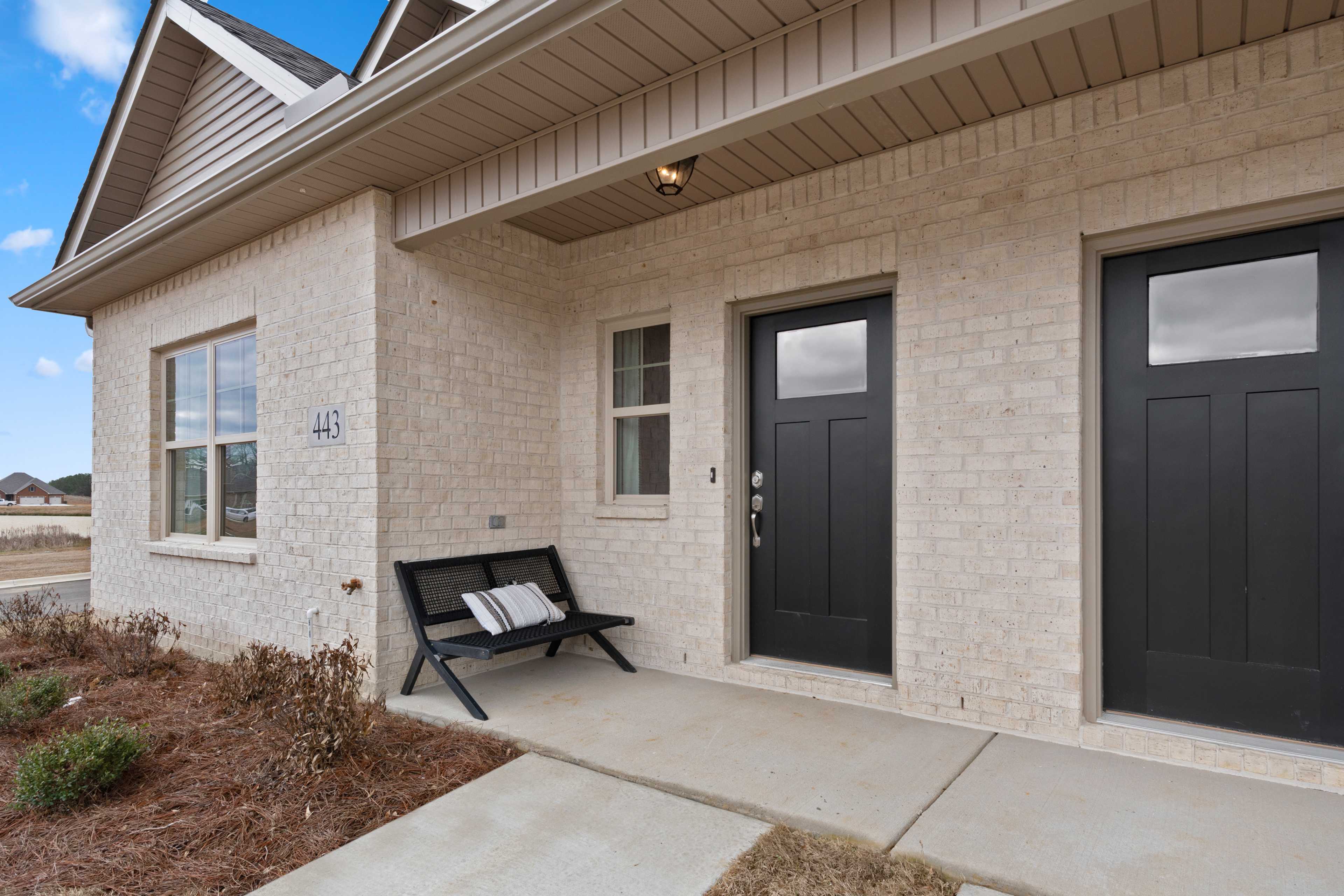 Beige brick home exterior at The Retreat at Cain Park in Hartselle Alabama with covered porch black doors and bench
