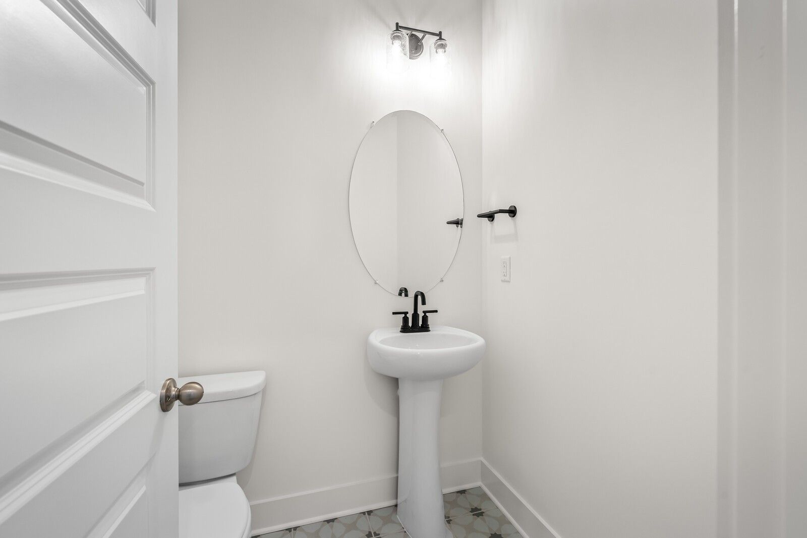 Bright powder room featuring white pedestal sink, round mirror, and toilet in Davidson Homes The Ash A, Gallatin, TN