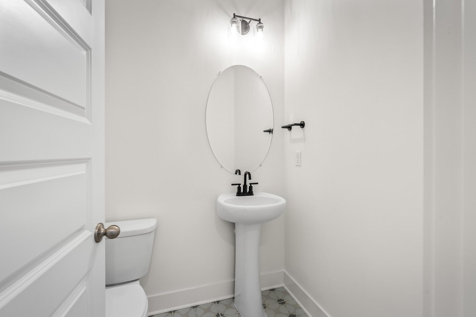 Bright powder room featuring white pedestal sink, round mirror, and toilet in Davidson Homes The Ash A, Gallatin, TN