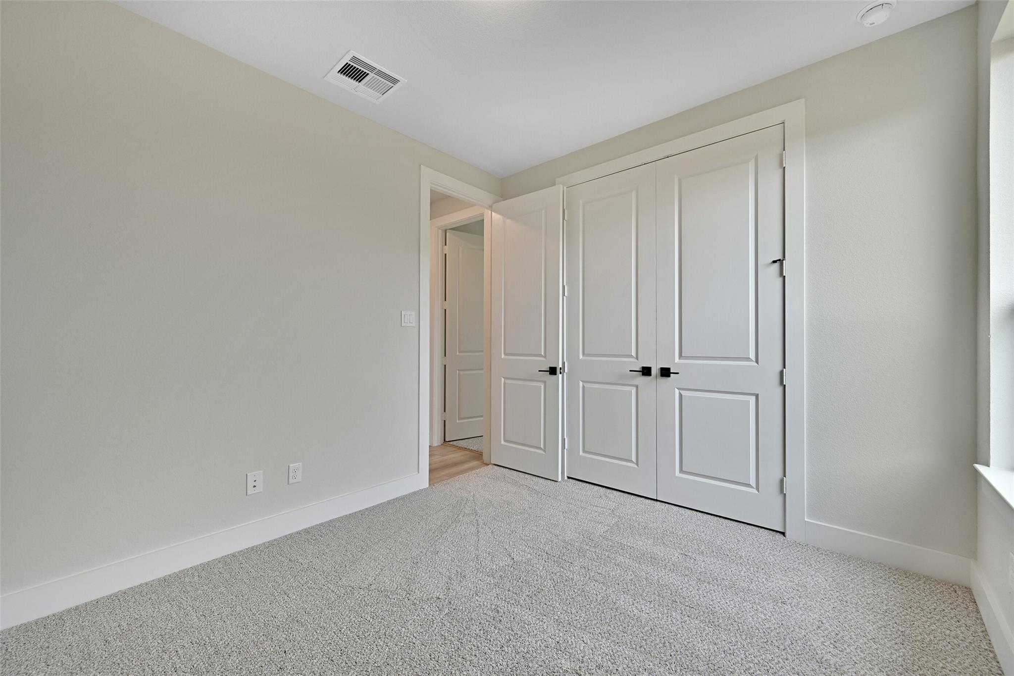 Spacious secondary bedroom with beige walls, carpet floor, double closet doors, and bathroom access in Davidson Homes The Edward C, Lago Mar, Texas City