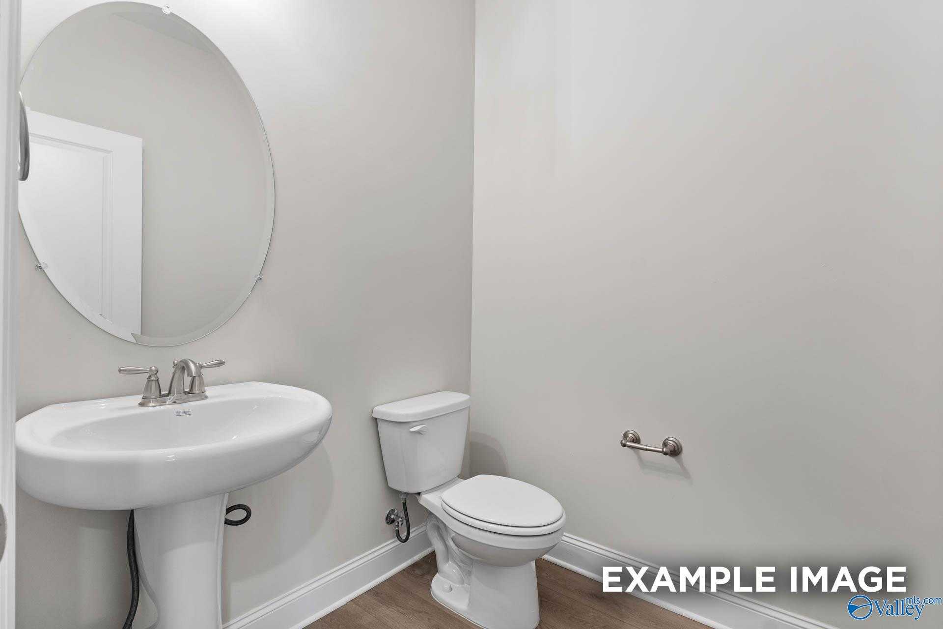 Elegant powder room with white pedestal sink, round mirror, and toilet in Davidson Homes The Finleigh, Meridianville, Alabama