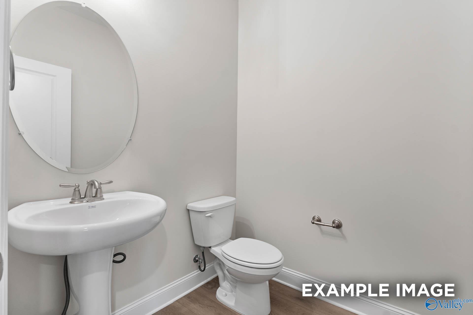 Modern powder room with round mirror, pedestal sink, and toilet in Davidson Homes The Finleigh, Huntsville, Alabama