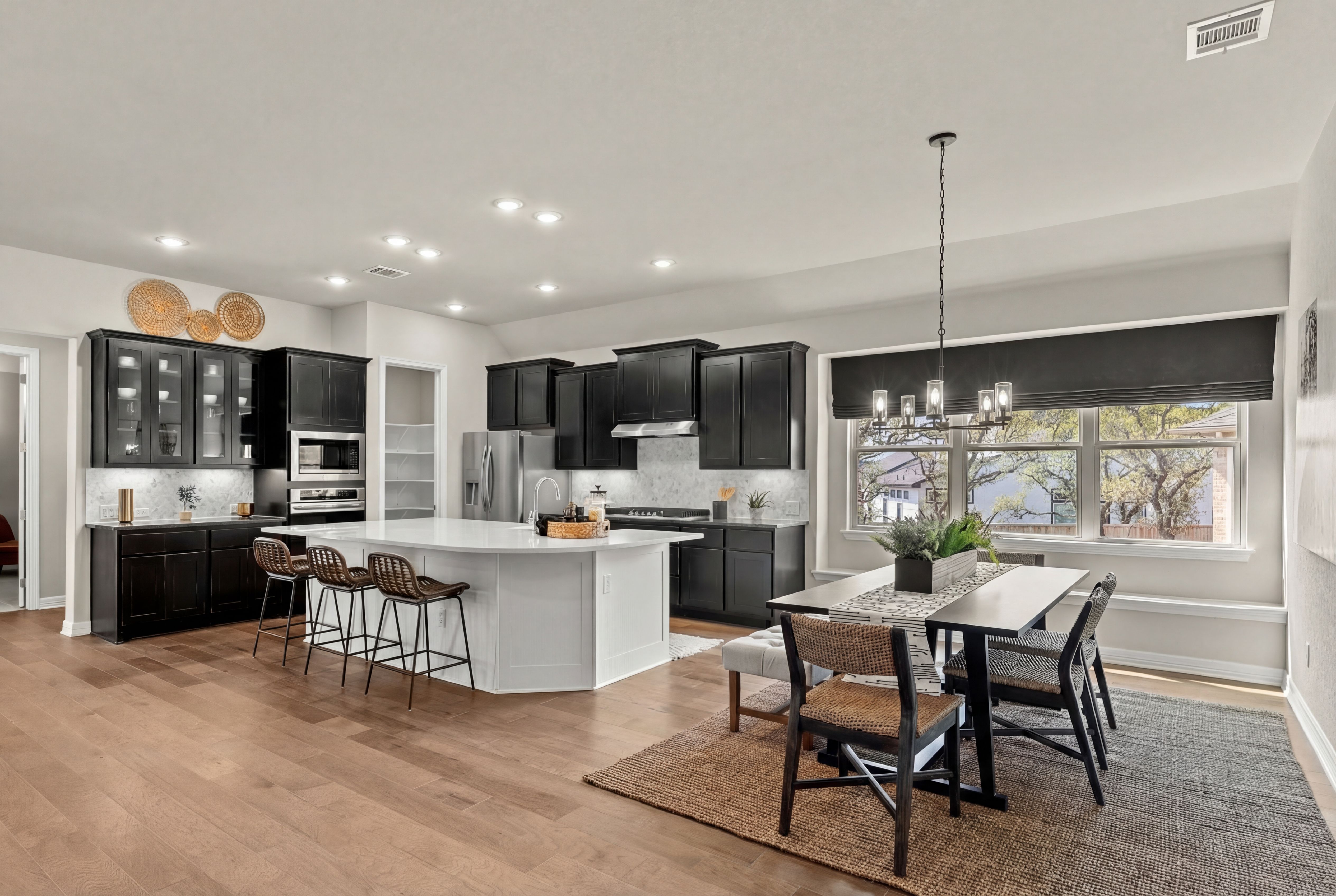 Modern open-concept kitchen dining area at Potranco Oaks in Castroville Texas with black cabinets quartz island hardwood floors