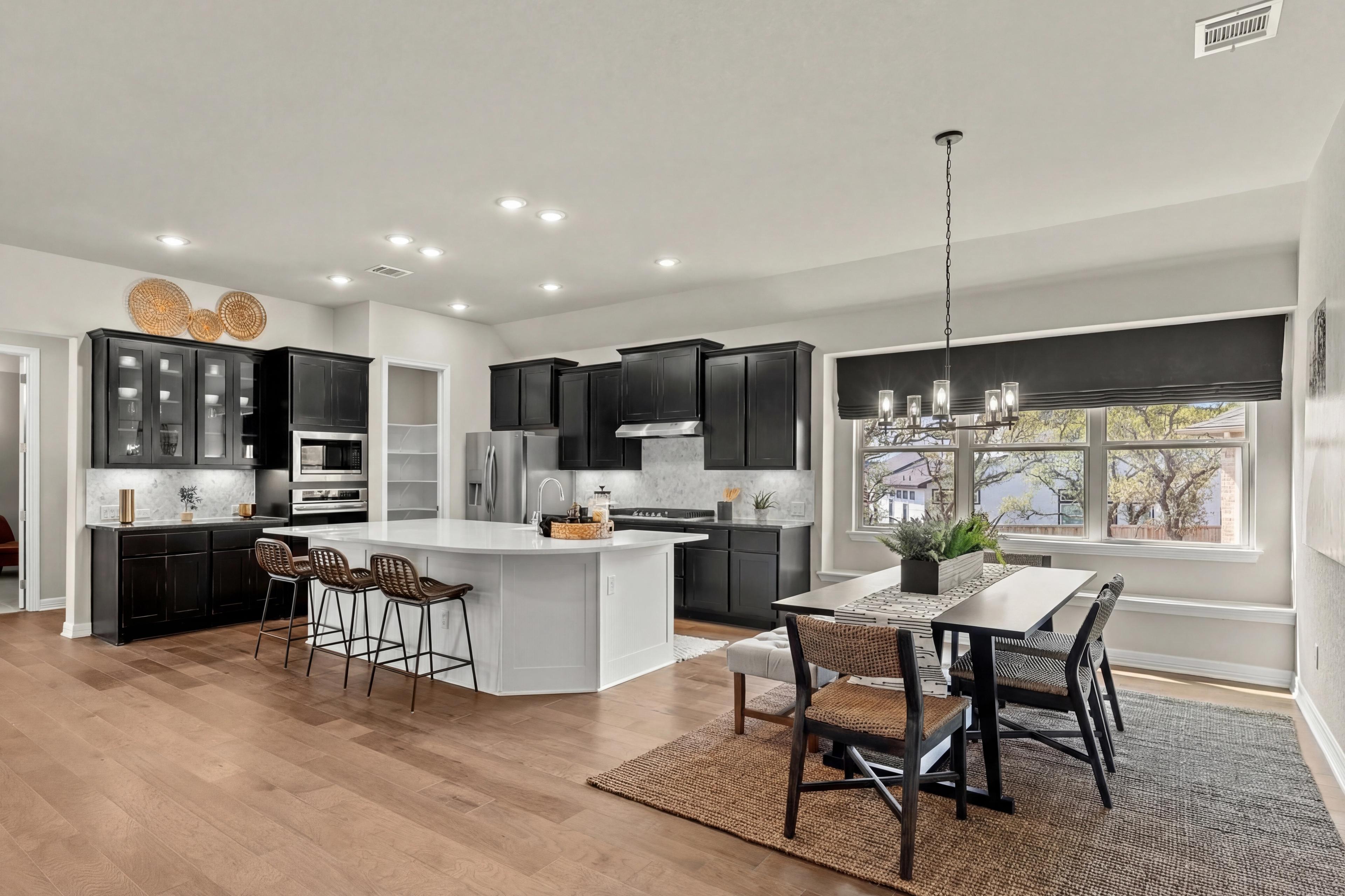 Modern open-concept kitchen dining area at Potranco Oaks in Castroville Texas with black cabinets quartz island hardwood floors