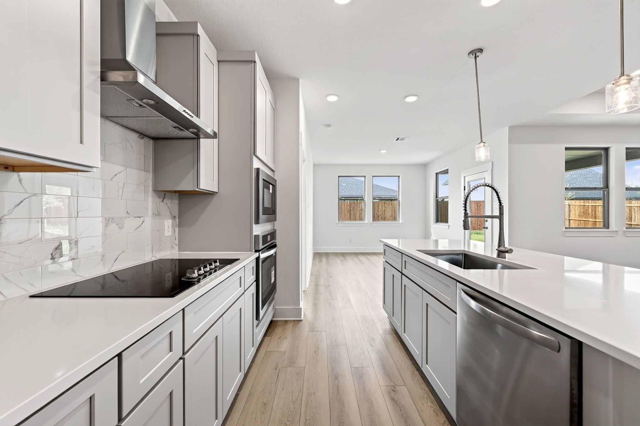 Modern kitchen with gray shaker cabinets, quartz countertops, marble tile backsplash, and island sink in The Holly F, Josephine, Texas