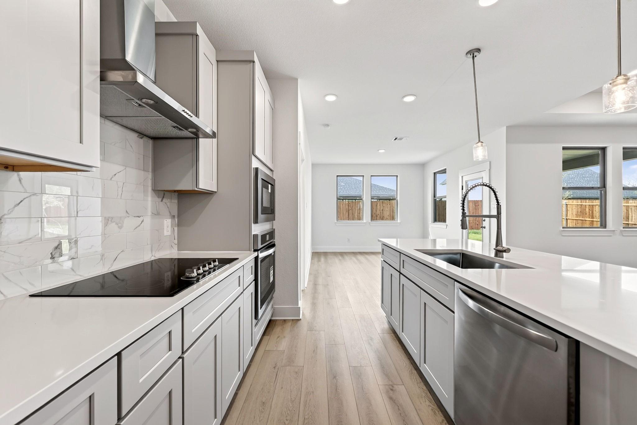 Modern kitchen with gray shaker cabinets, quartz countertops, marble tile backsplash, and island sink in The Holly F, Josephine, Texas