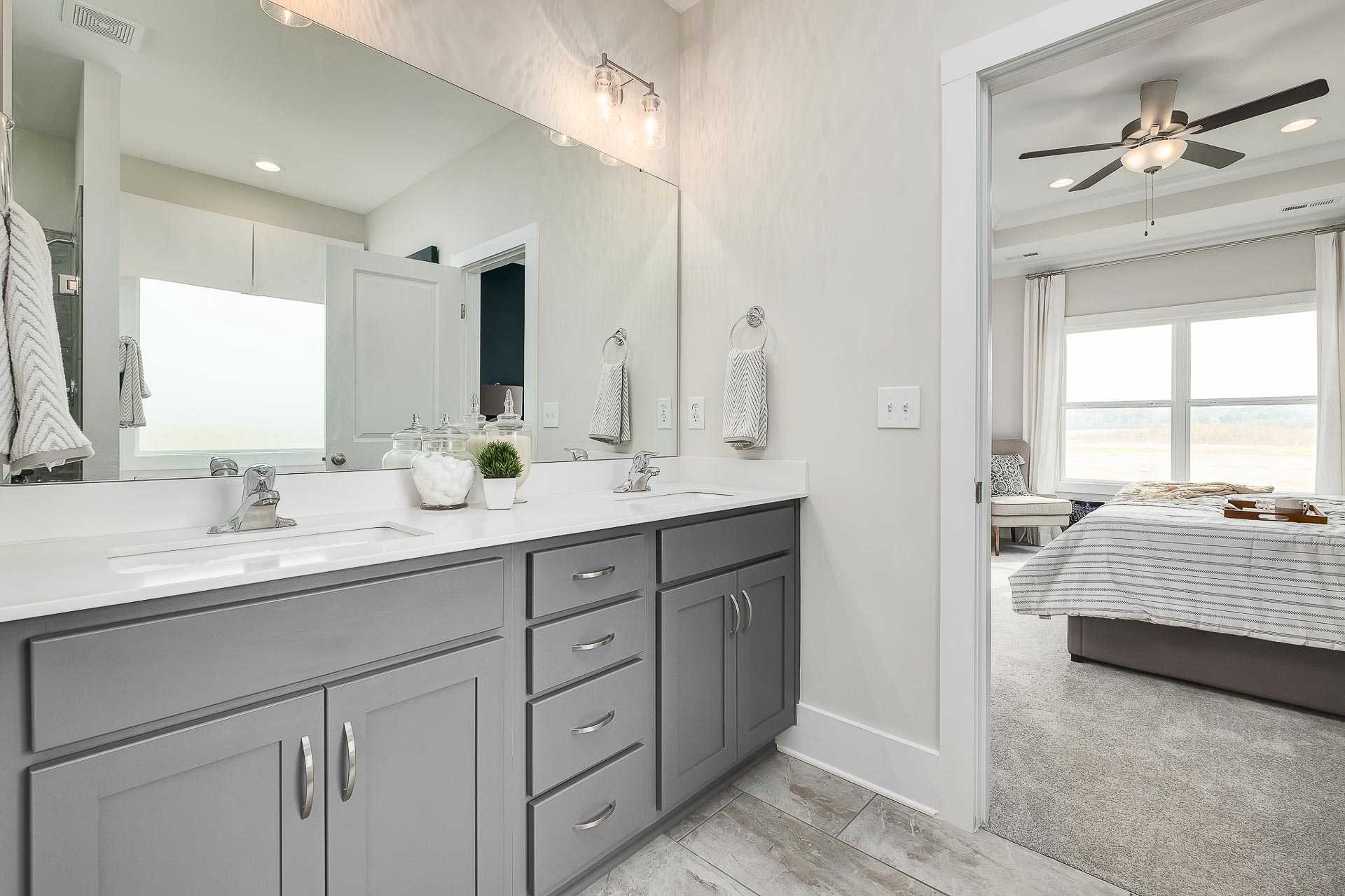 Spacious master bathroom in The Everett C featuring gray double vanity, large mirror, and adjacent bedroom view