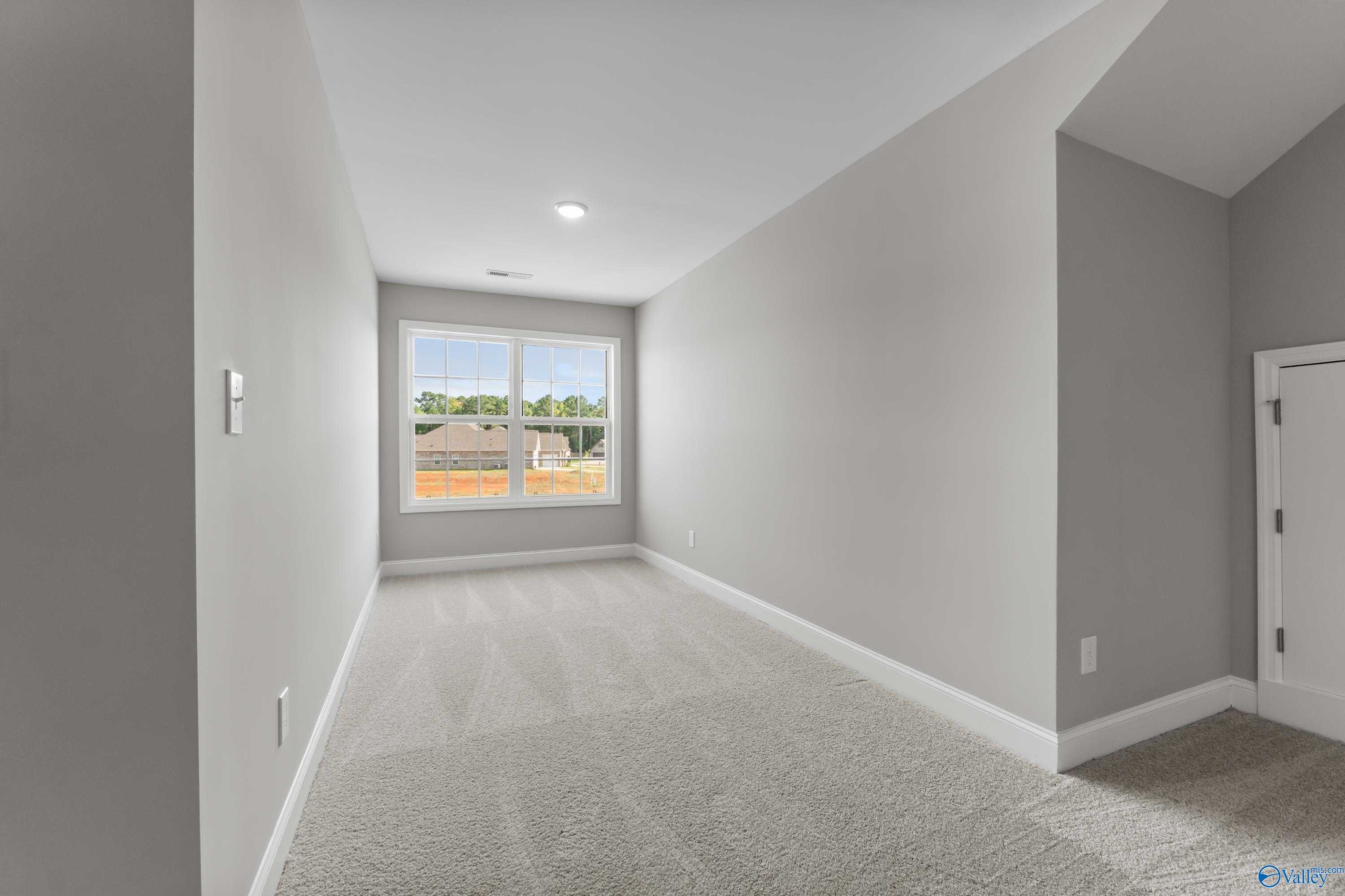 Bright empty bedroom with large window, gray walls, and plush carpet in Davidson Homes The Rockford, Harvest AL