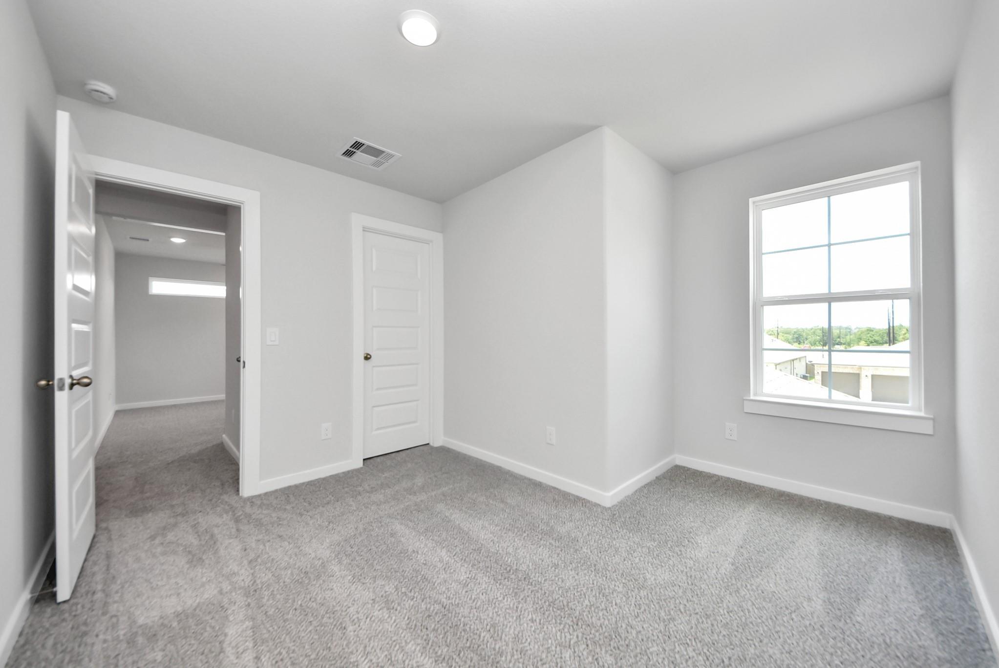 Bright bedroom with plush carpet and window in The Sabine E floor plan by Davidson Homes in Windmill Estates, Magnolia.