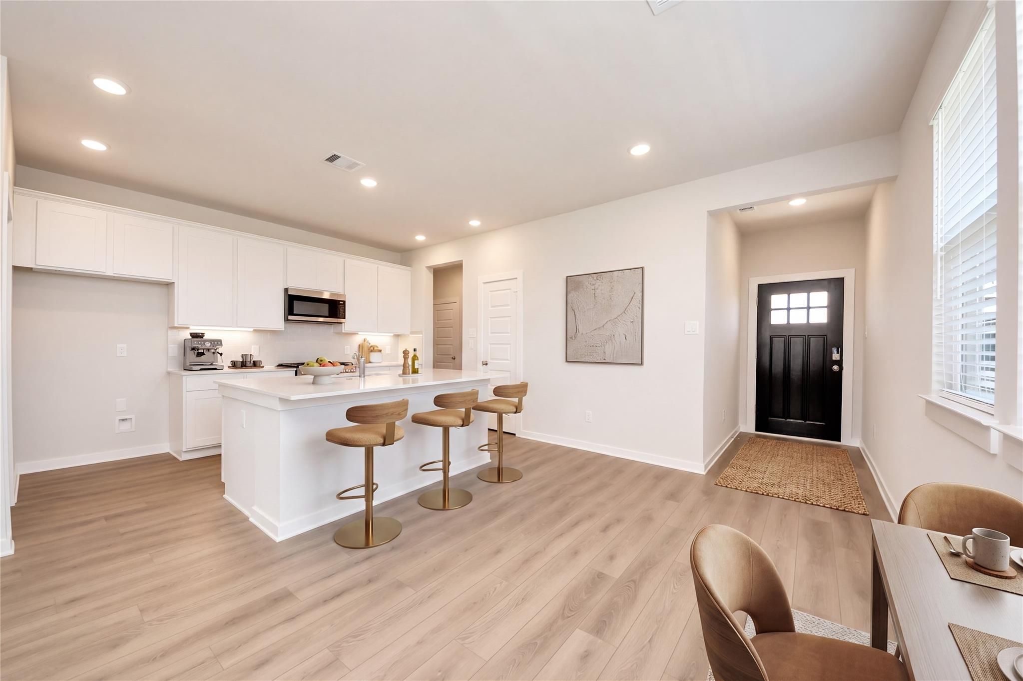 Open-concept kitchen with white cabinetry, island with barstools, and light wood floors in Davidson Homes The Costa A, Beasley, TX