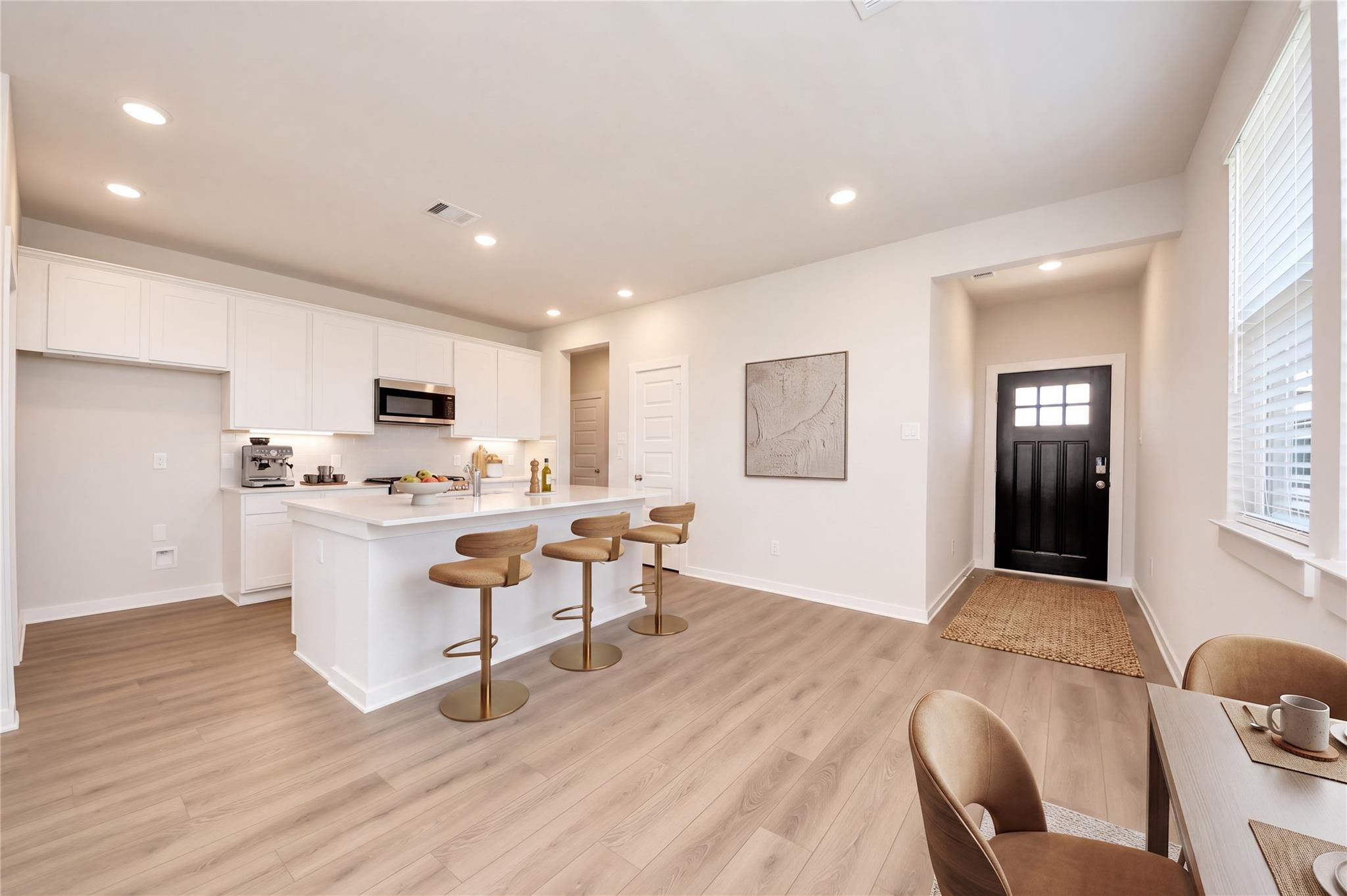 Open-concept kitchen with white cabinetry, island with barstools, and light wood floors in Davidson Homes The Costa A, Beasley, TX